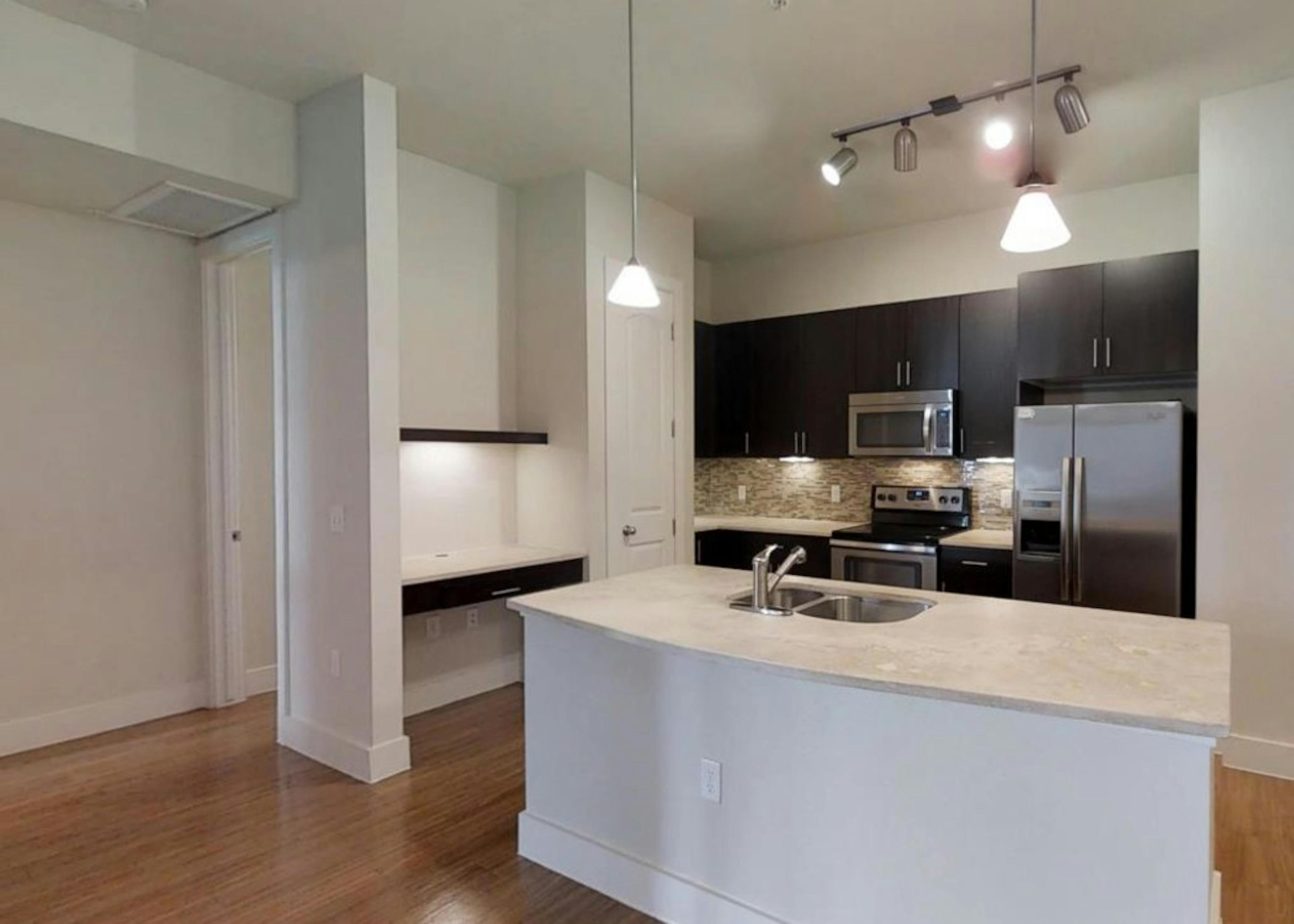 A view of a kitchen at AMLI Ridgegate apartments with a granite counter top island and hard wood floor with overhead lighting