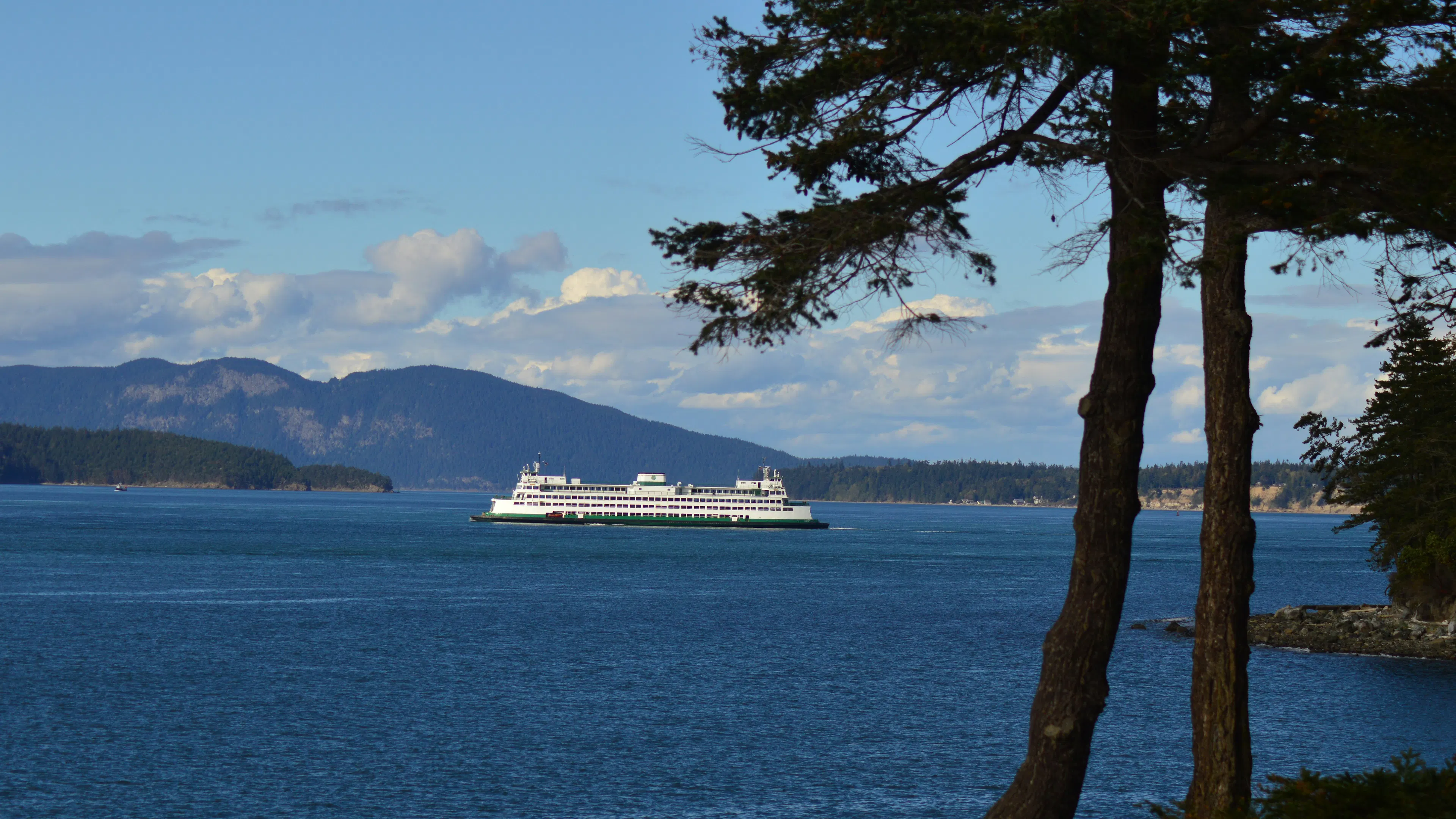 A Washington State Ferry traveling between two forest covered islands with mountains in the background