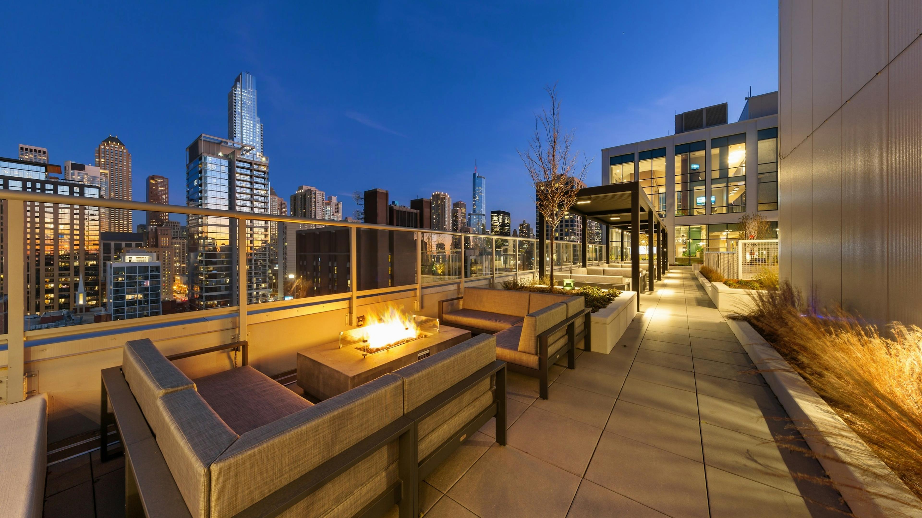 Fire pit in middle of two beige outdoor couches on AMLI 808 rooftop at night surrounded by vibrant city buildings