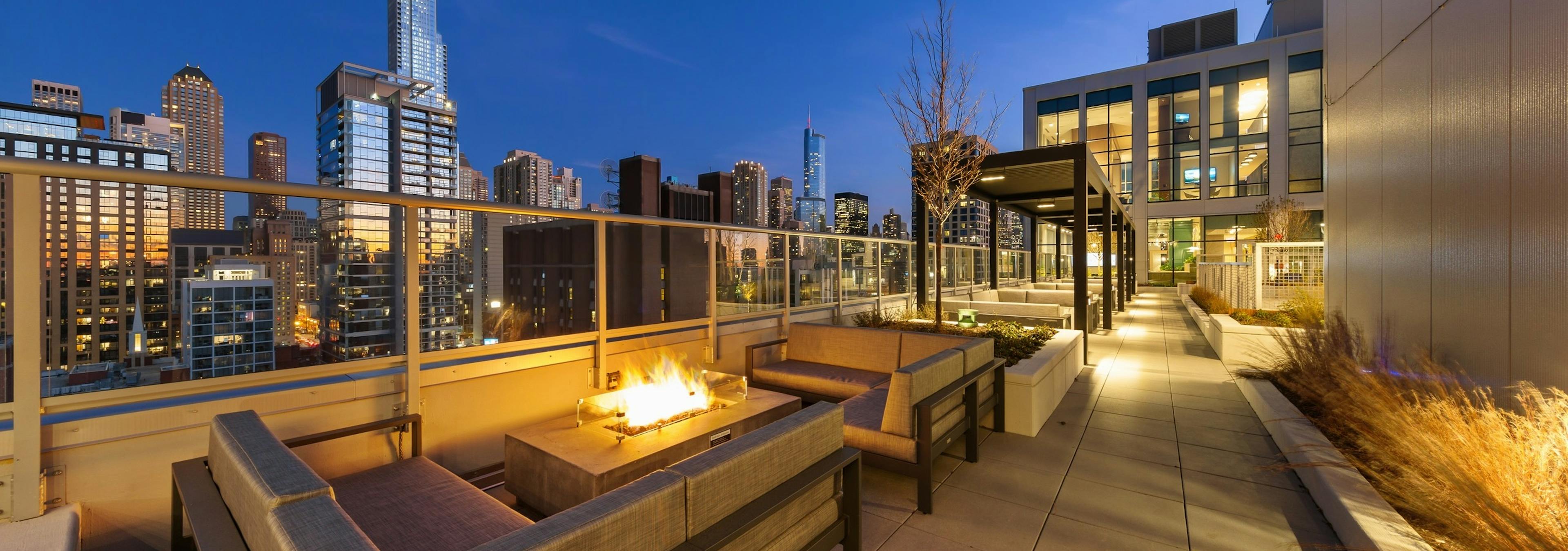 Fire pit in middle of two beige outdoor couches on AMLI 808 rooftop at night surrounded by vibrant city buildings