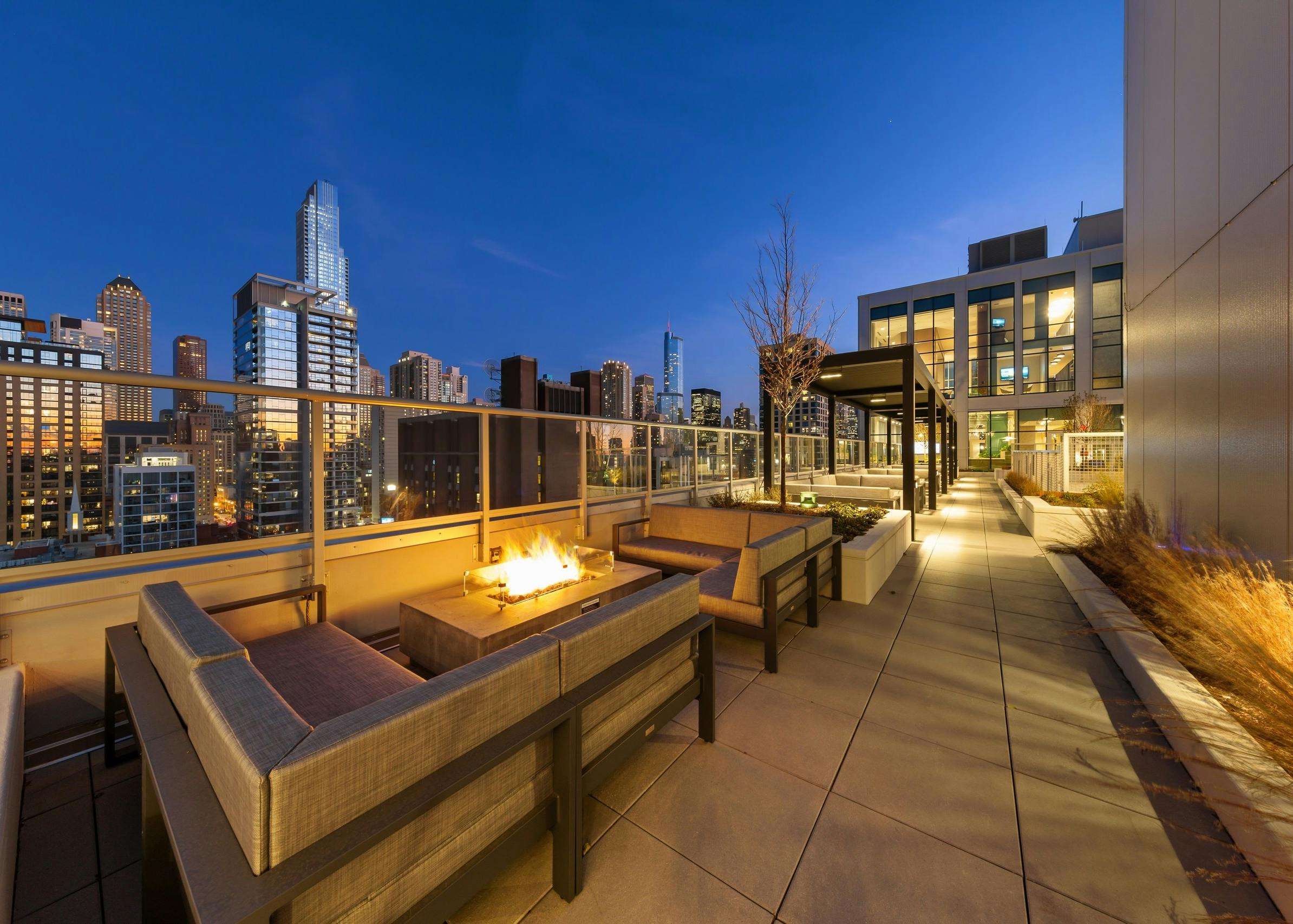 Fire pit in middle of two beige outdoor couches on AMLI 808 rooftop at night surrounded by vibrant city buildings