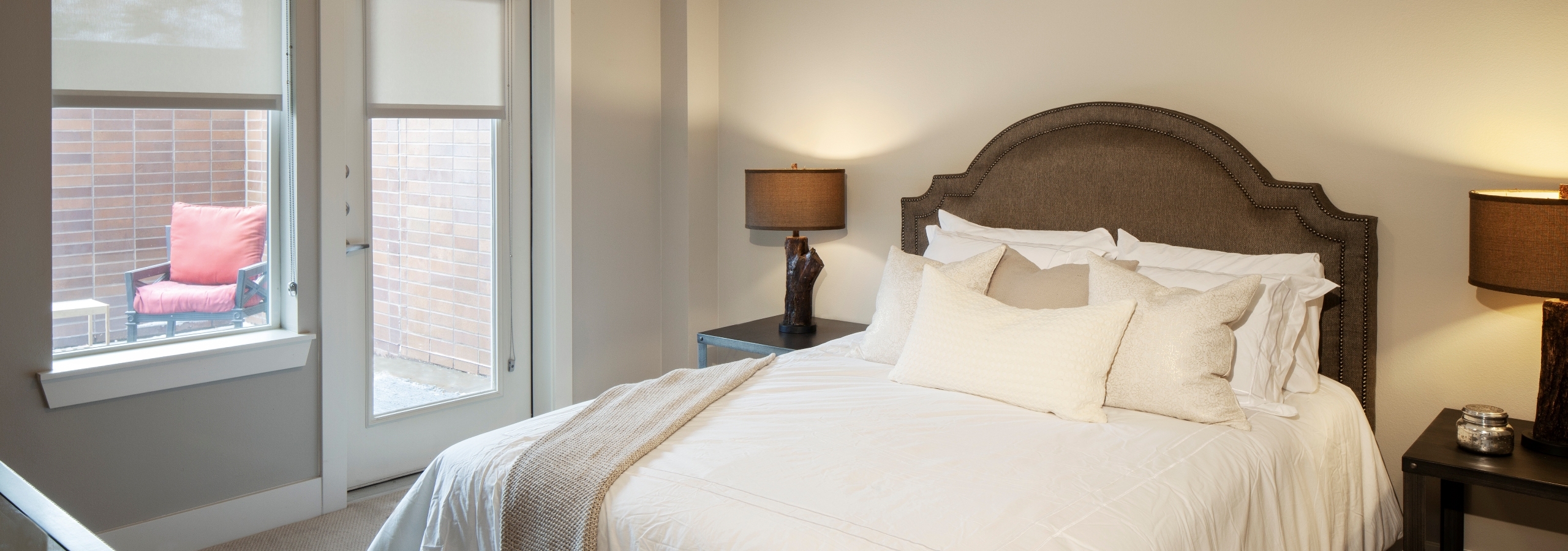 A bedroom at AMLI Riverfront Green apartments with view of bedside tables as well as view of bedroom accessible outdoor deck
