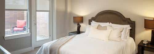 A bedroom at AMLI Riverfront Green apartments with view of bedside tables as well as view of bedroom accessible outdoor deck