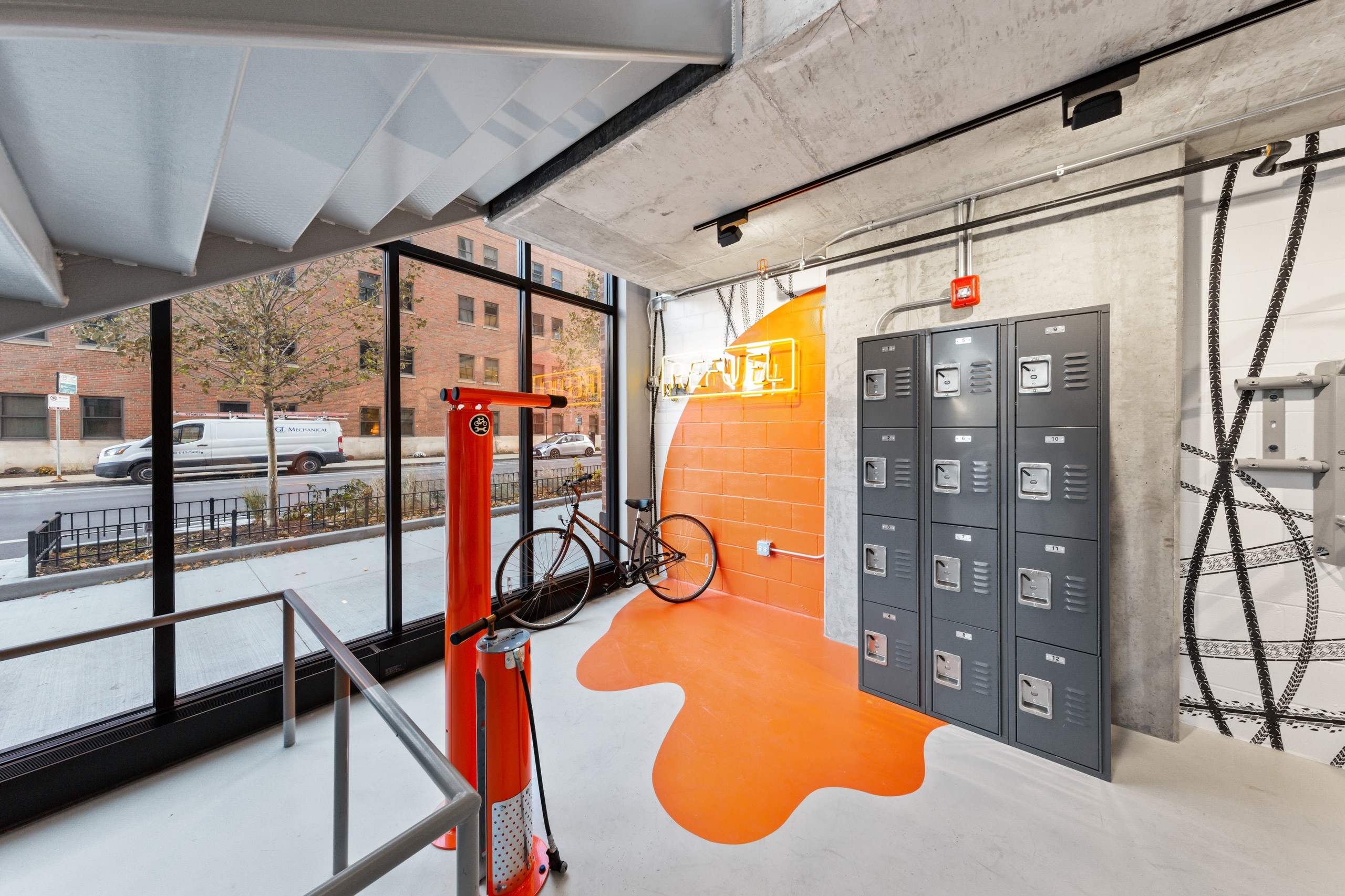 AMLI 808 bike room featuring stacked lockers and a red air pump with a vibrant orange accent on surrounding grey walls
