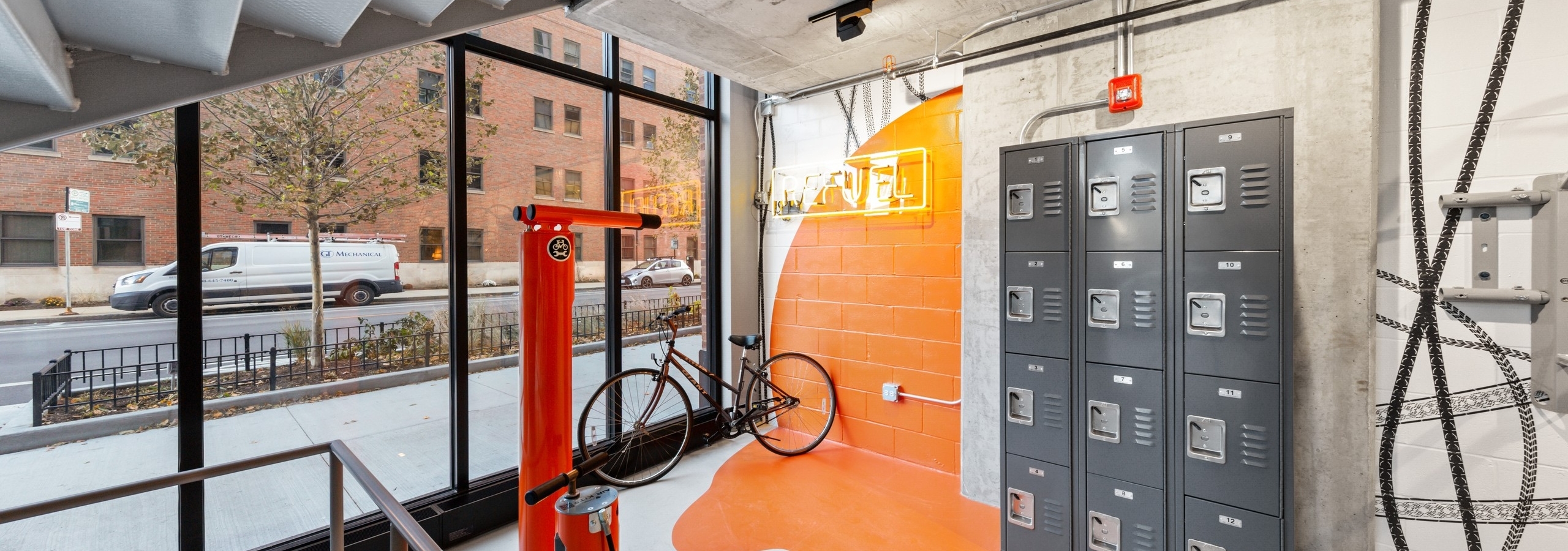 AMLI 808 bike room featuring stacked lockers and a red air pump with a vibrant orange accent on surrounding grey walls