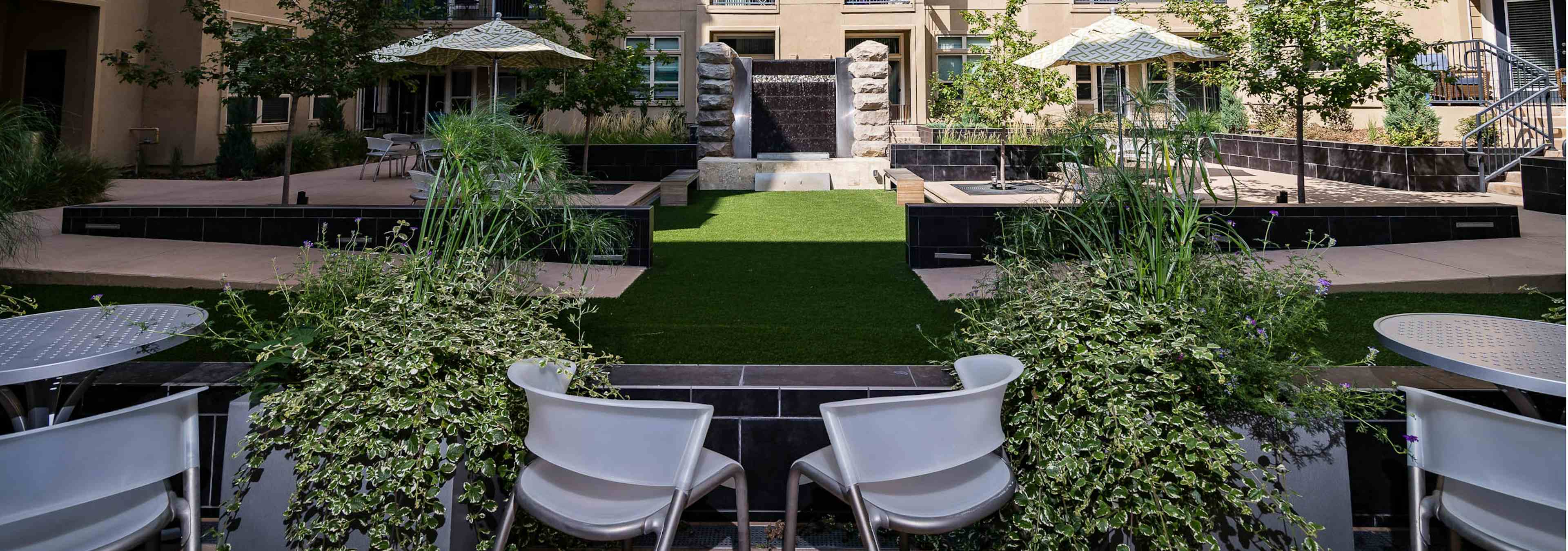 Daytime exterior view of AMLI RidgeGate courtyard centered view surrounding trees and plants facing cascading stone waterfall