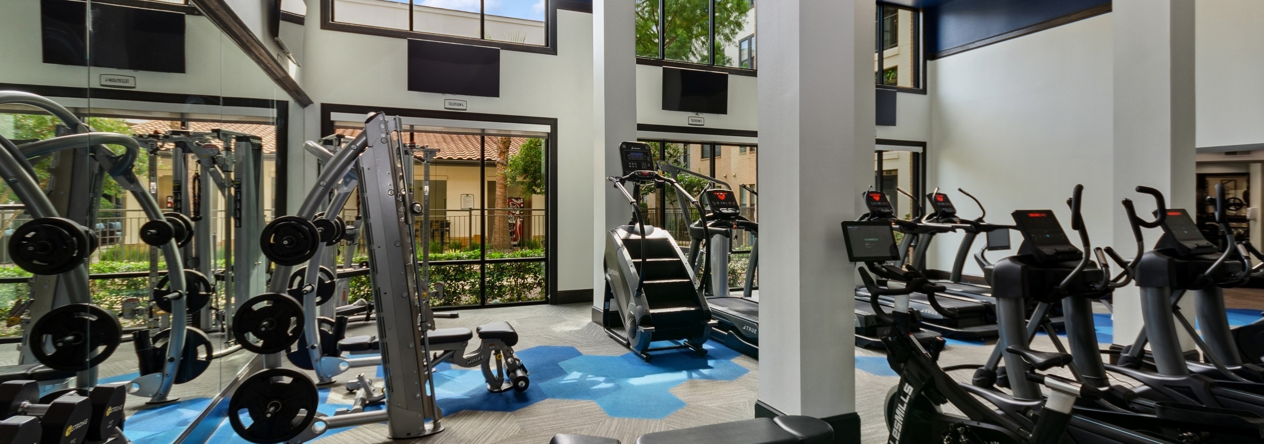 AMLI Campion Trail fitness center with treadmills and cardio machines and mounted TVs and large two-story windows