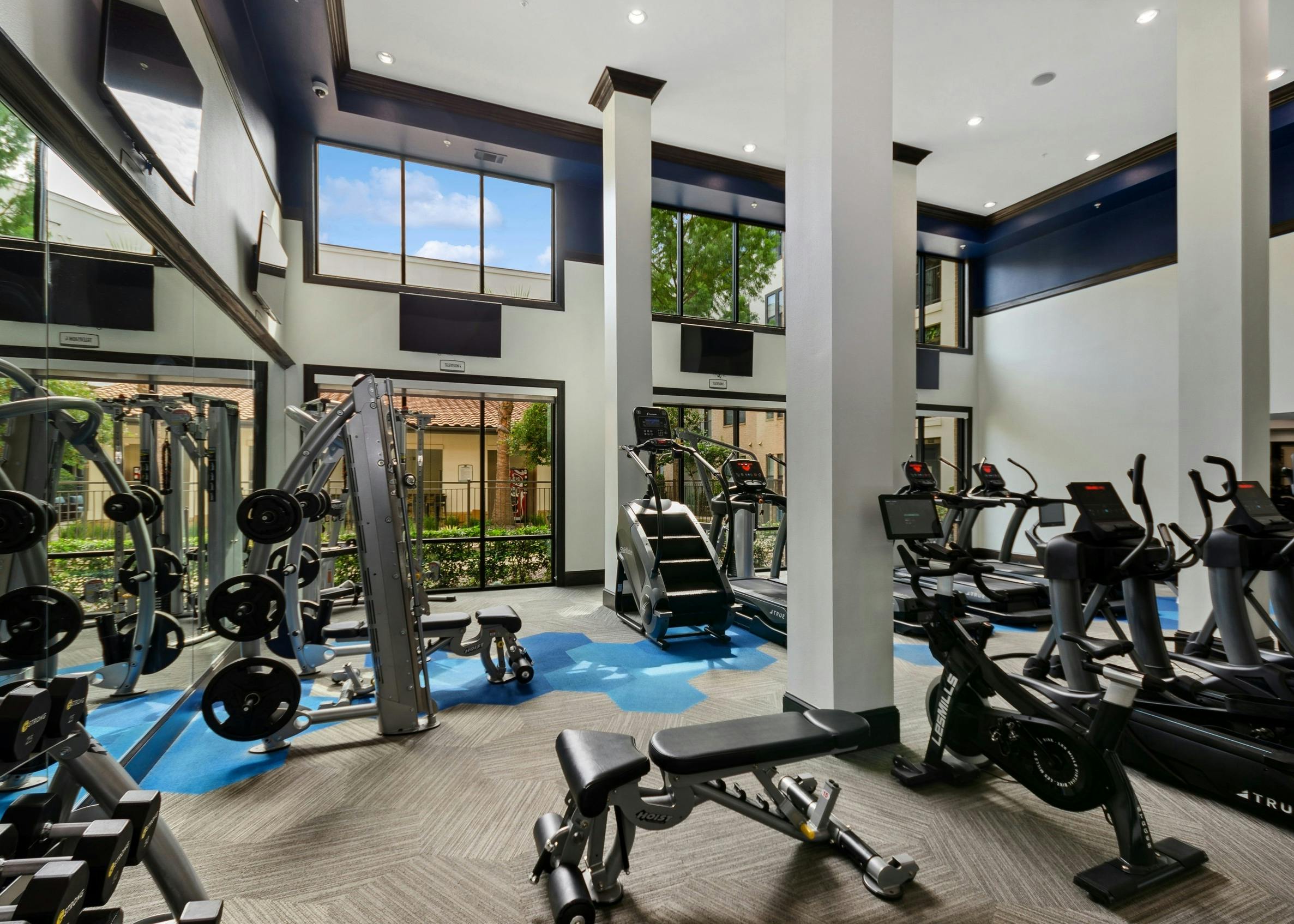 AMLI Campion Trail fitness center with treadmills and cardio machines and mounted TVs and large two-story windows