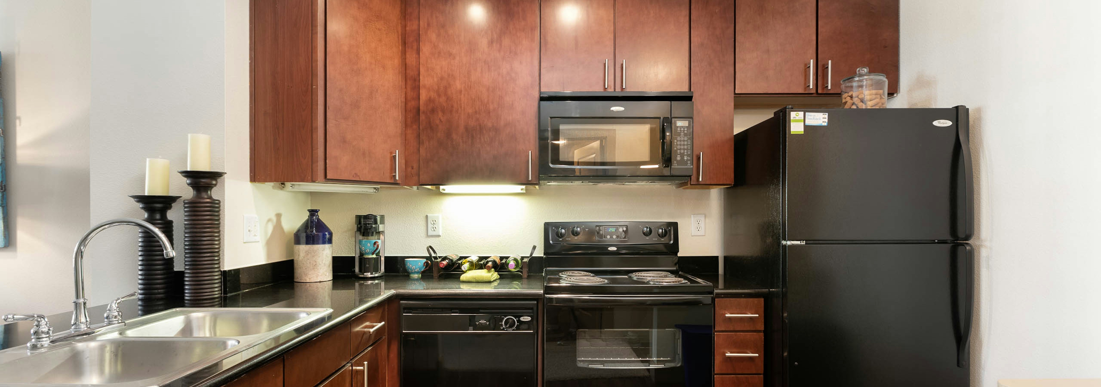 AMLI Eastside kitchen with black appliances and cherry cabinetry with stainless steel sink and tall candlesticks on counter