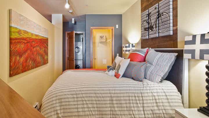 Interior view of a AMLI 535 apartment bedroom with a large queen-sized bed and a screen printed painting of a bicycle above