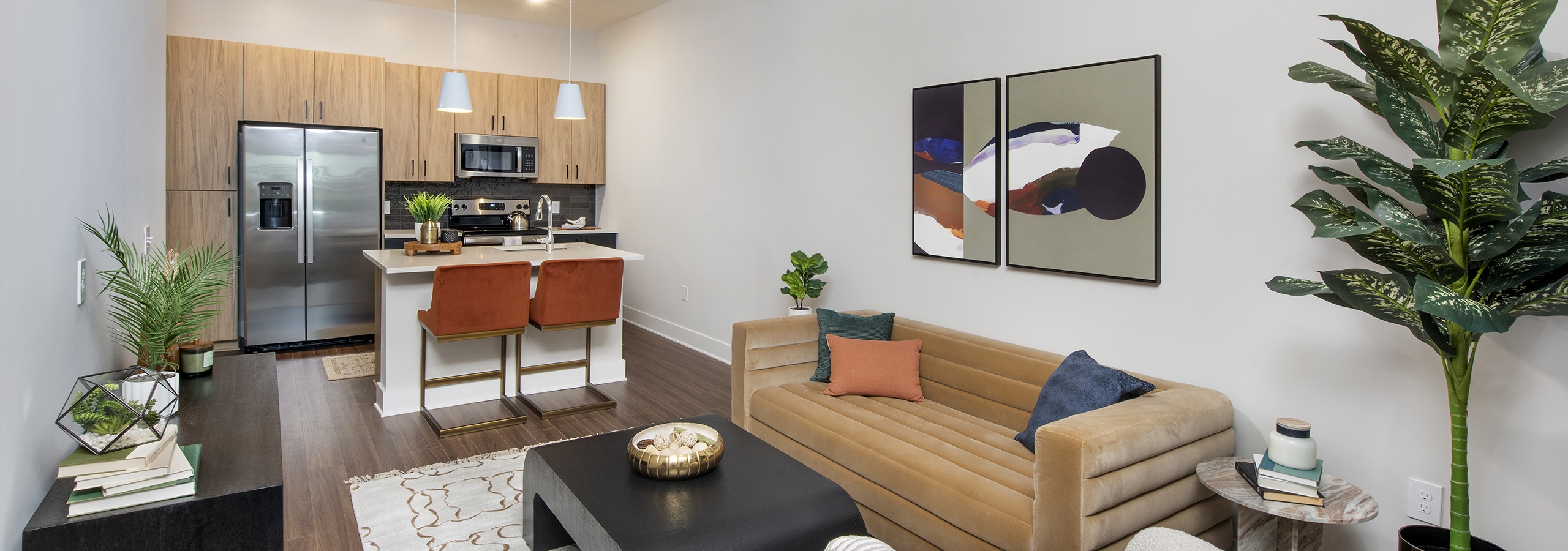 AMLI Flatiron living room with wood floors and tan couch with white chair and dark wood accent tables with view to kitchen