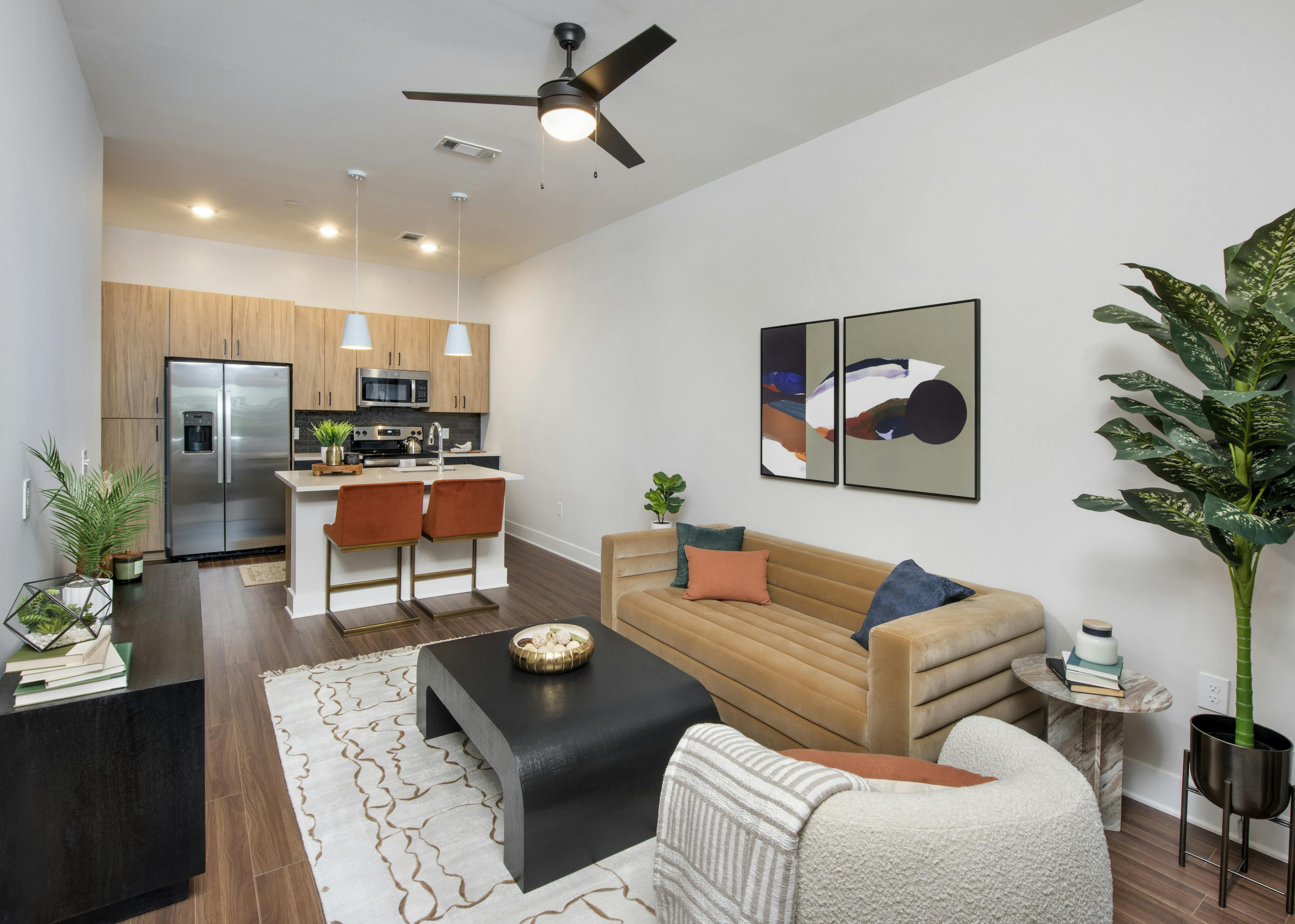 AMLI Flatiron living room with wood floors and tan couch with white chair and dark wood accent tables with view to kitchen