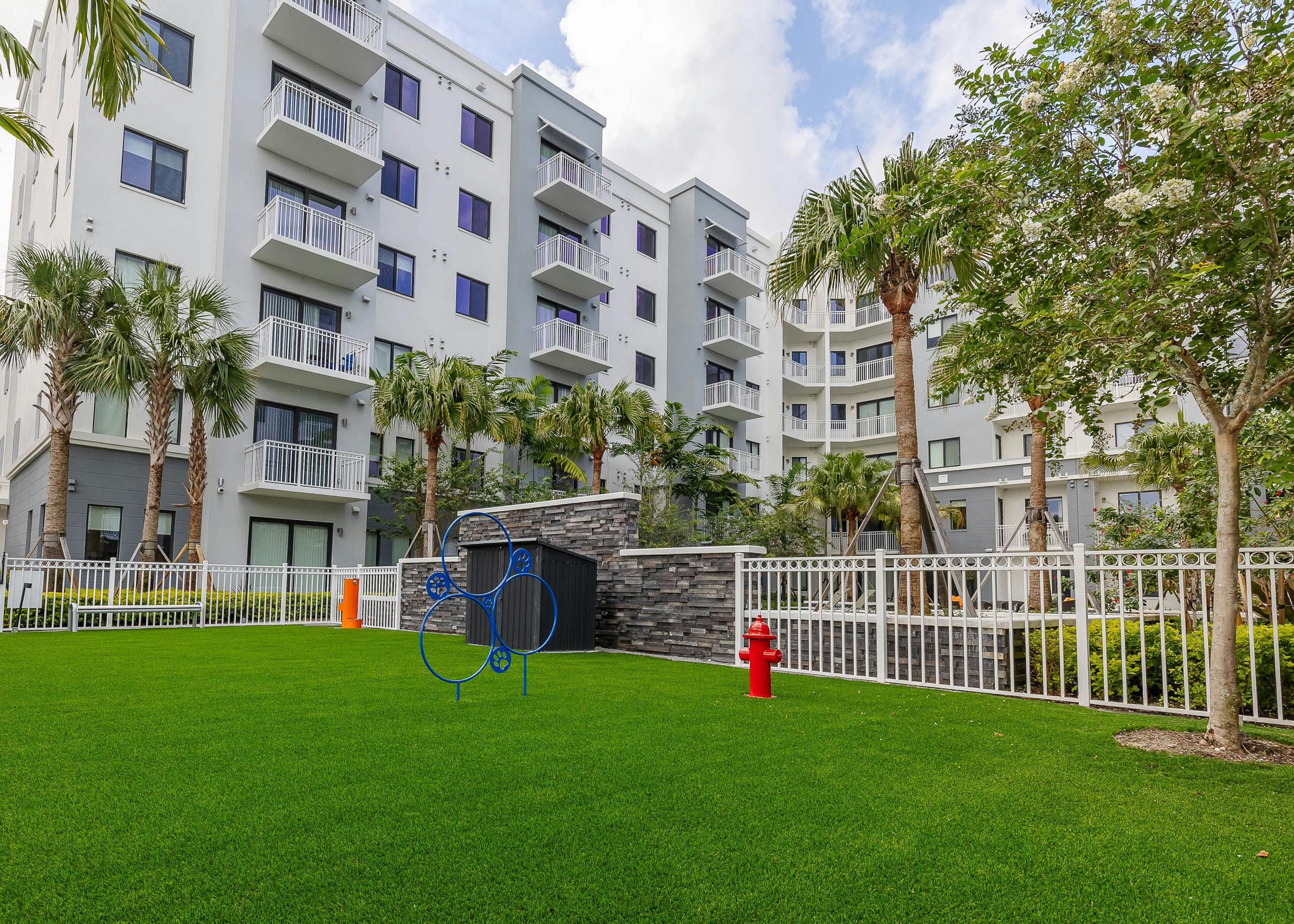 Exterior view of AMLI Park West apartments dog park with faux green grass and agility equipment and an orange water station