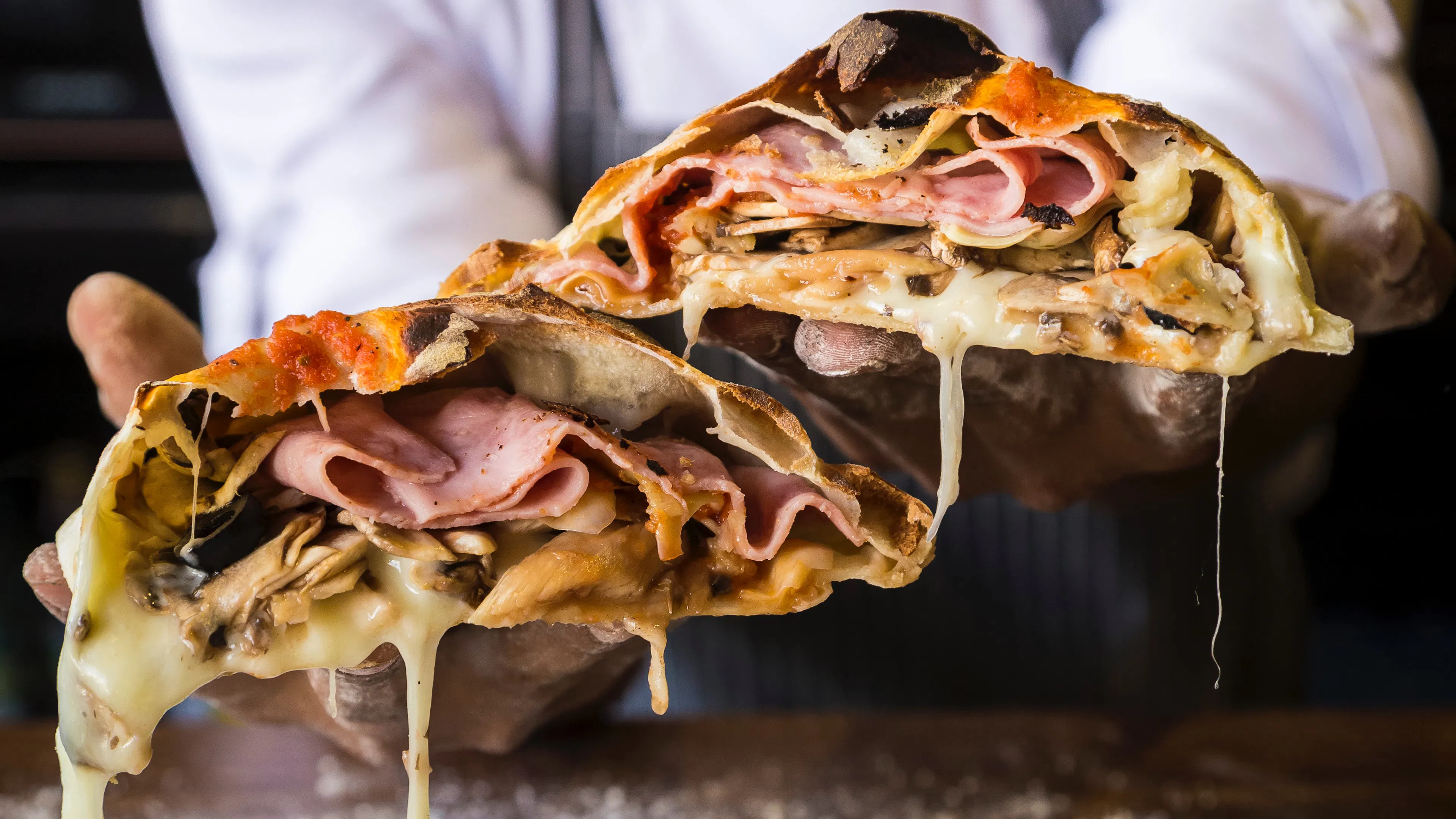 a chef holding out a stromboli cut in half with melted cheese and meats