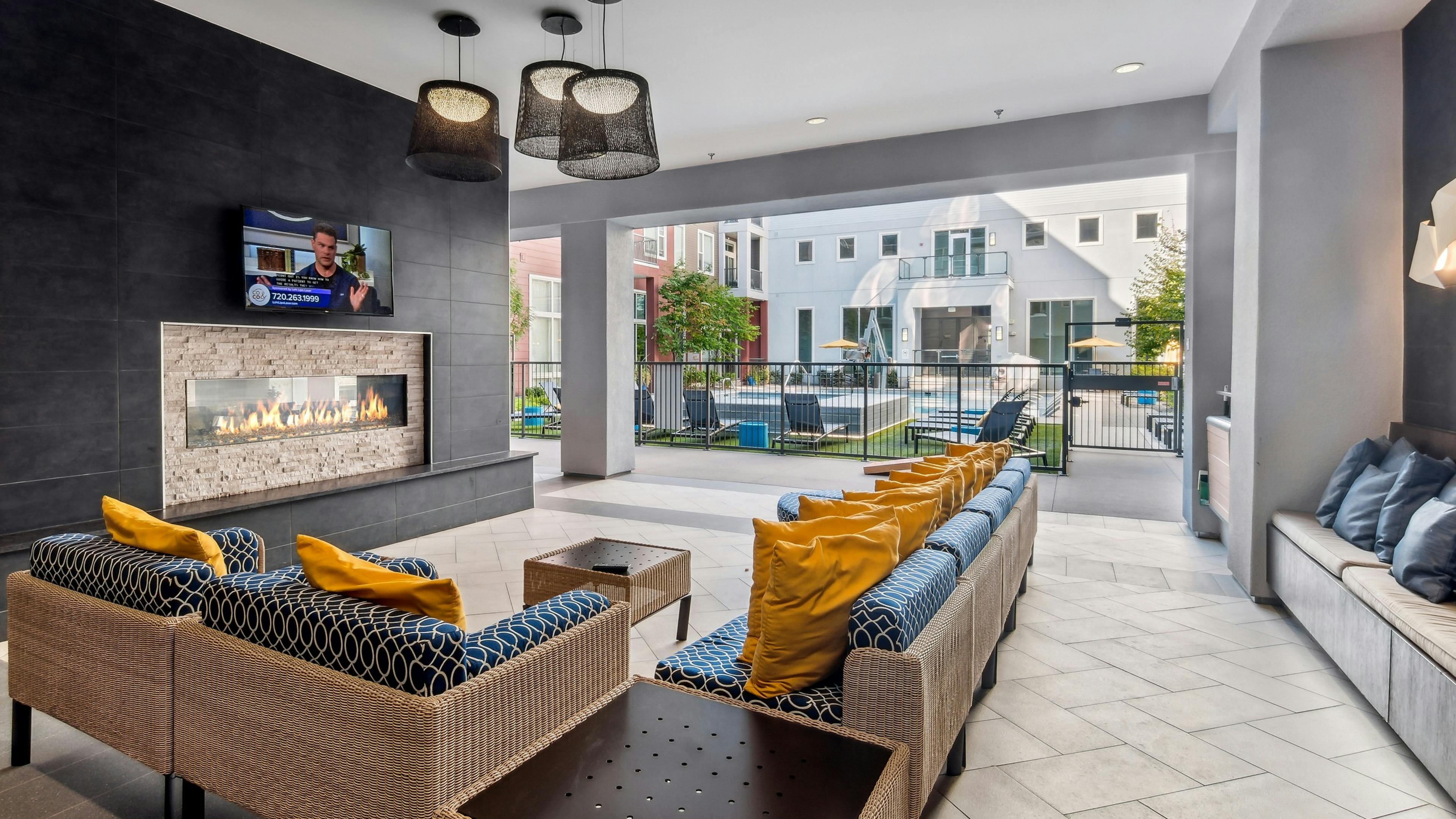 Outdoor living room with couches with big yellow pillows and fireplace and TV at AMLI Denargo Market with view of the pool