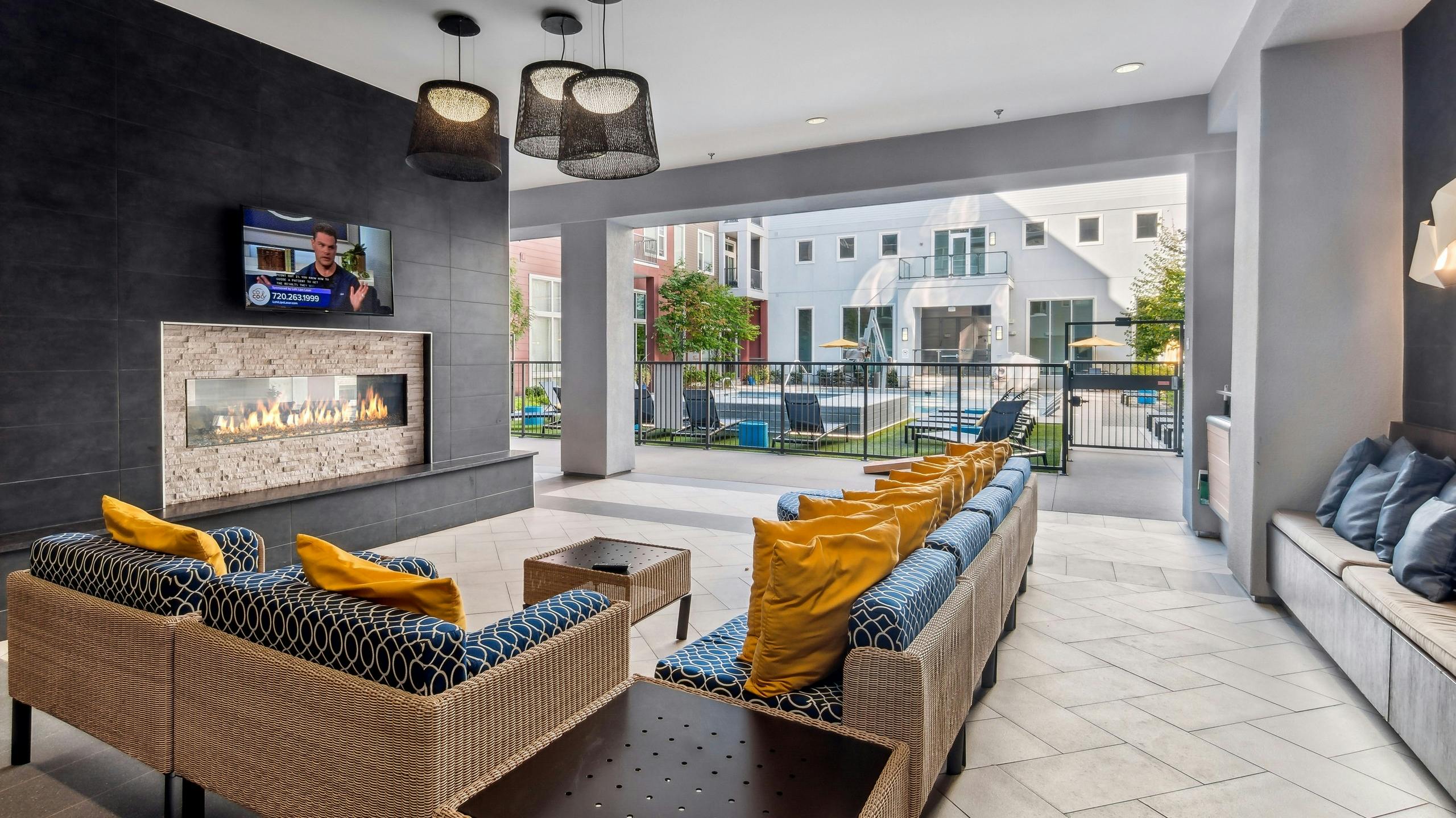 Outdoor living room with couches with big yellow pillows and fireplace and TV at AMLI Denargo Market with view of the pool