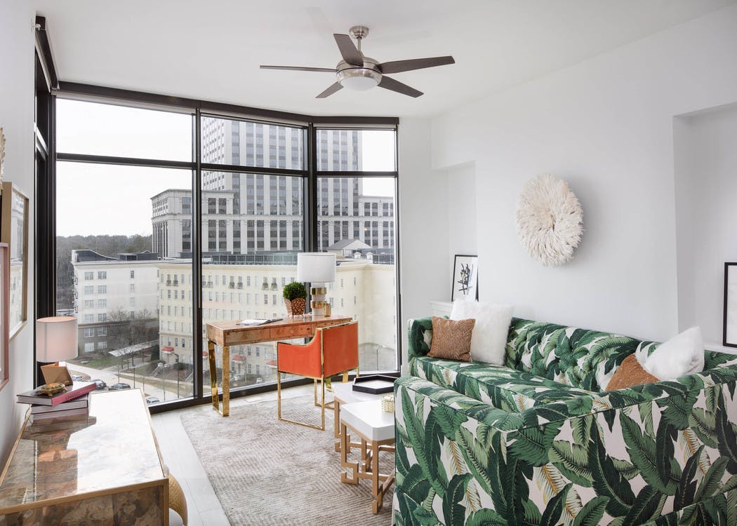 Interior of AMLI 3464 living room with white walls and floor to ceiling windows with a bold palm tree branch printed sofa
