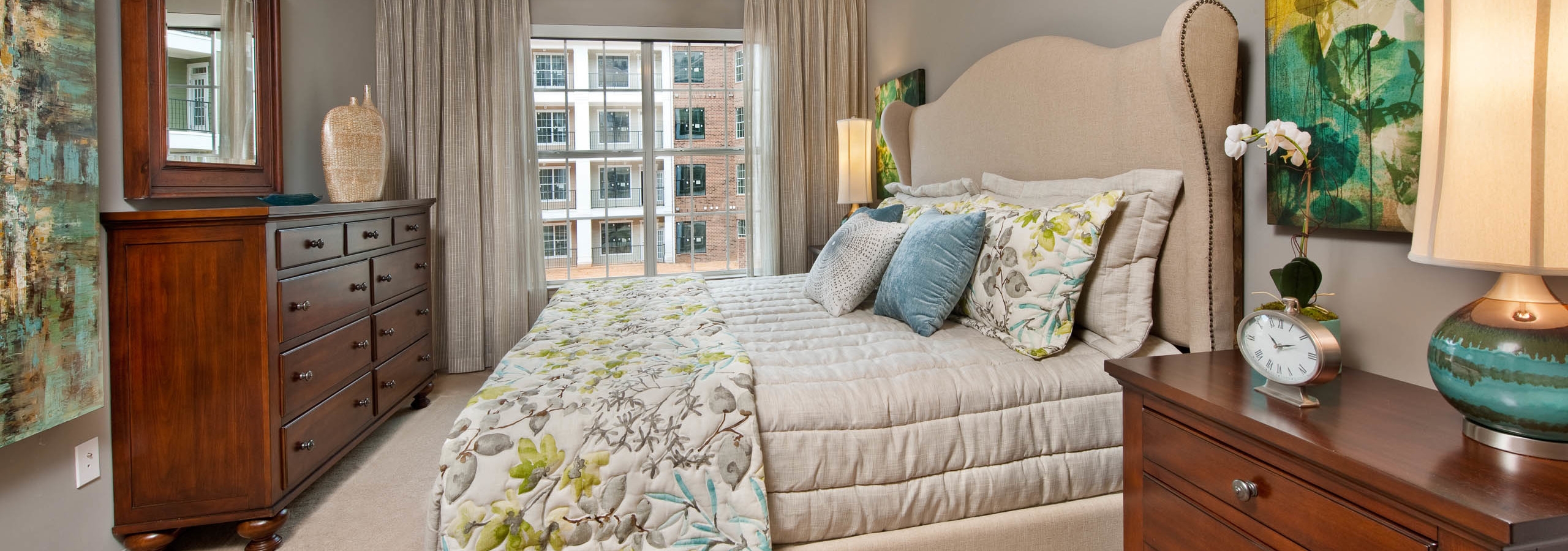 Bedroom at AMLI North Point with a large window and white carpeted floors and decorated with neutral colors and teal accents