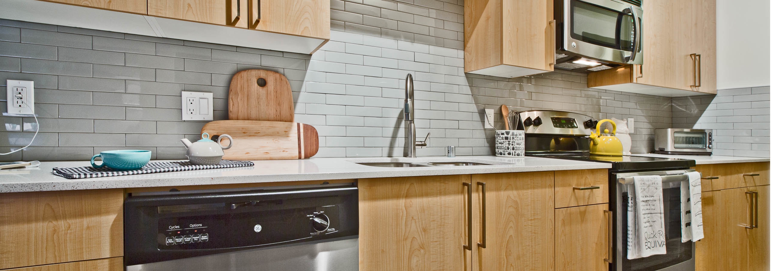 Interior view of AMLI Mark24 apartment kitchen with light cabinets white quartz counter tops and grey back splash