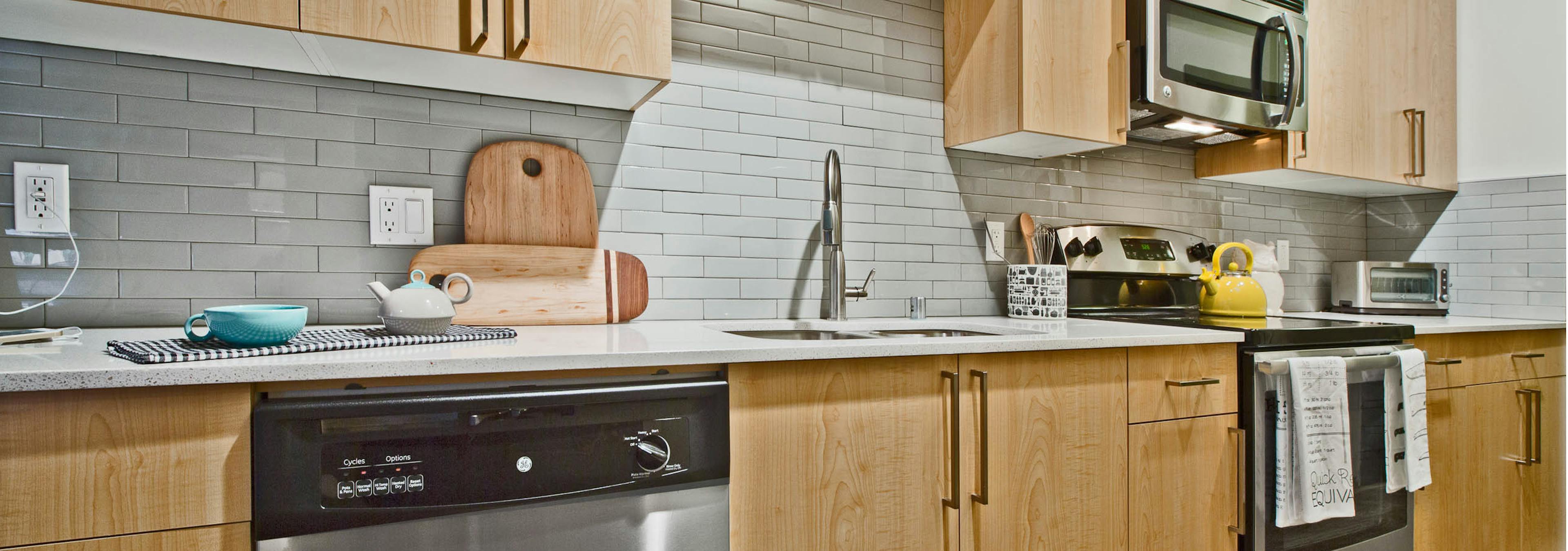 Interior view of AMLI Mark24 apartment kitchen with light cabinets white quartz counter tops and grey back splash  