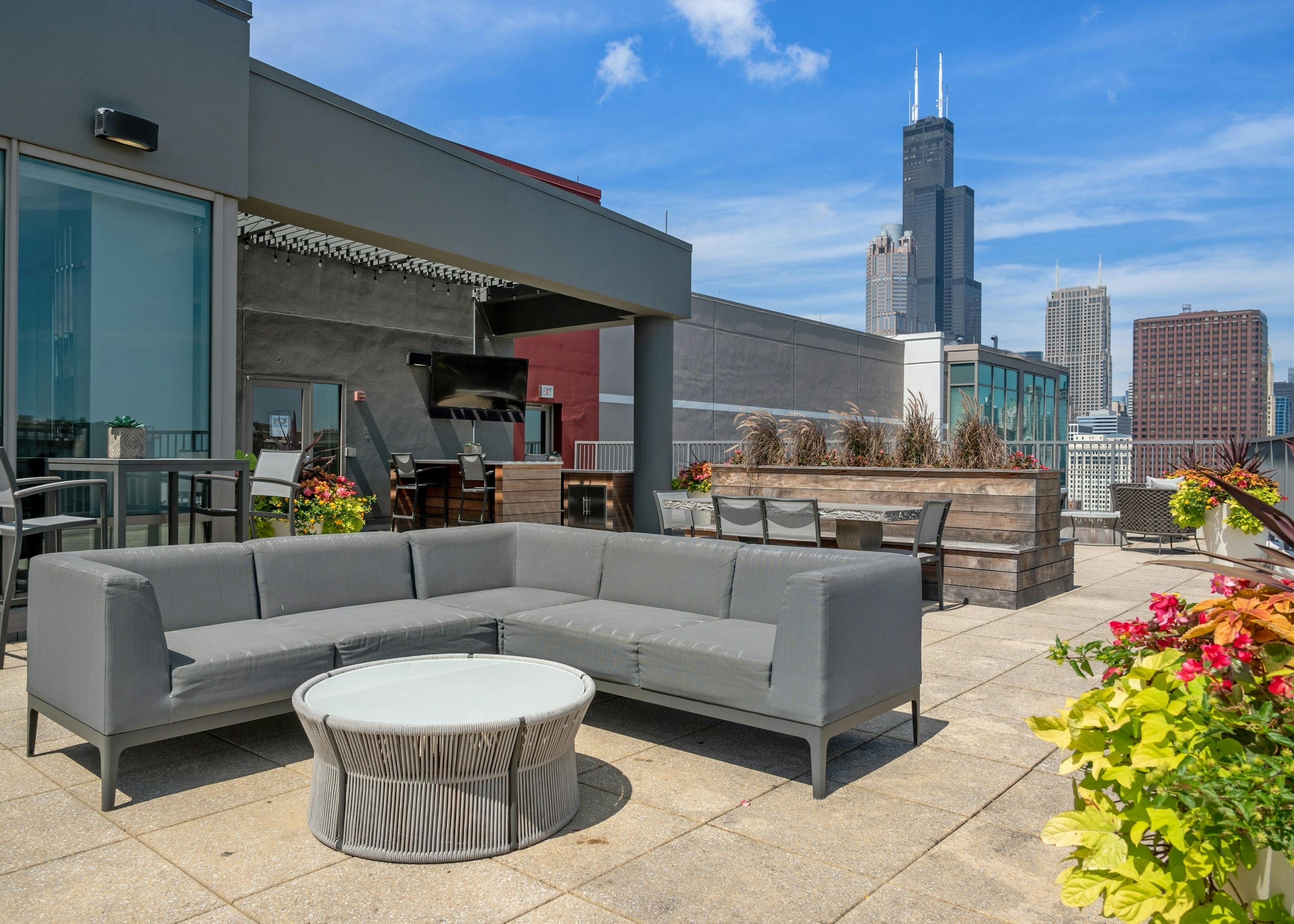 AMLI 900 rooftop with grey sectional couch and round table on concrete patio with wood planters and flowers and city skyline view