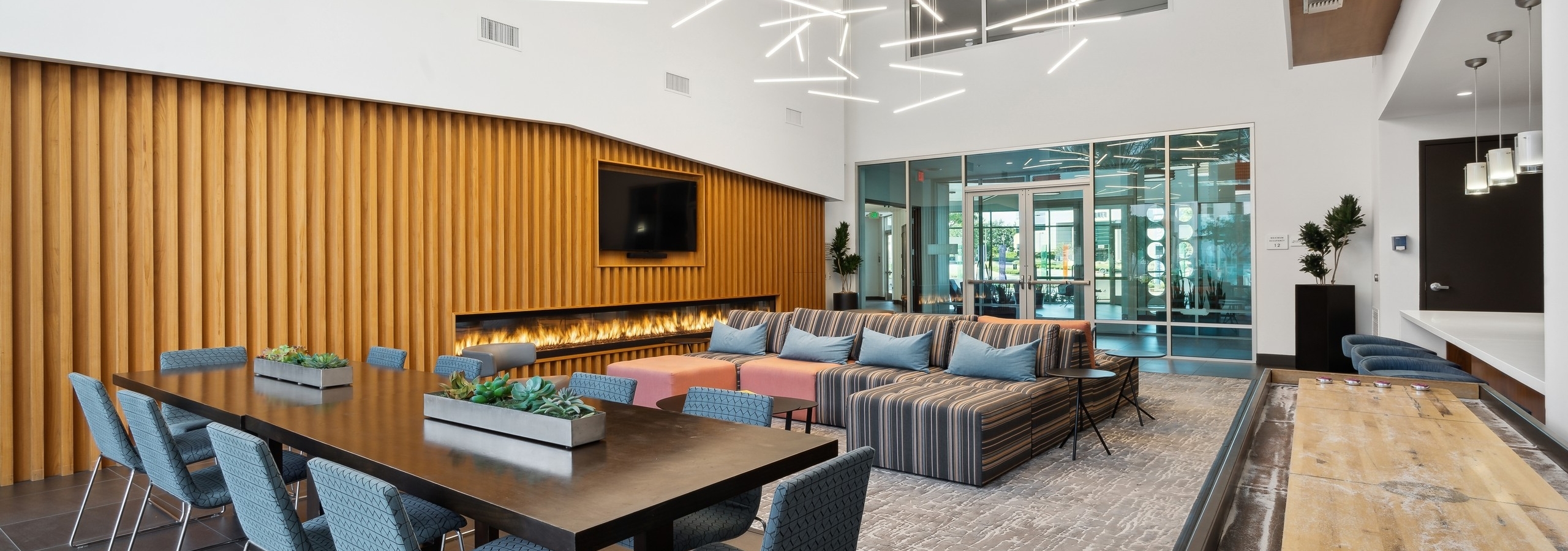 AMLI Uptown Orange clubroom with large dining table with chairs and couches and shuffleboard and lit fireplace
