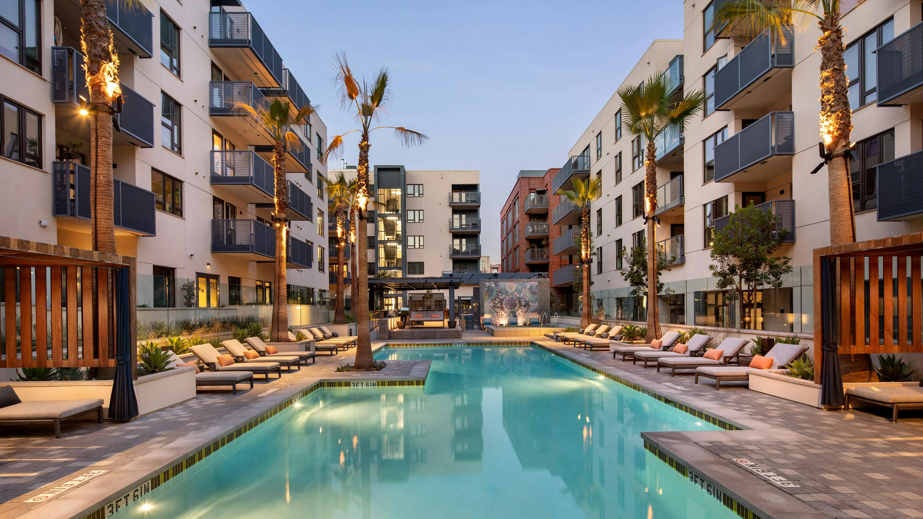 Courtyard lit swimming pool with lounge seating and palm trees and an elevated jacuzzi at dusk at AMLI Old Pasadena apartments