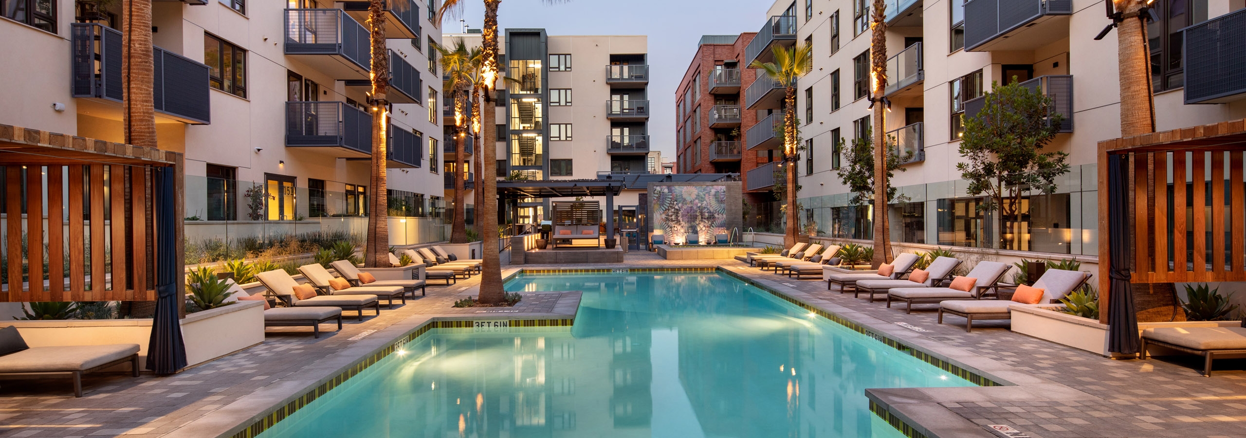 Courtyard lit swimming pool with lounge seating and palm trees and an elevated jacuzzi at dusk at AMLI Old Pasadena apartments