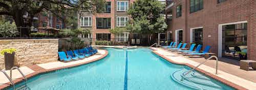 Close up of swimming pool at AMLI Eastside apartment community with blue lounge chairs and view facing brick building facade
