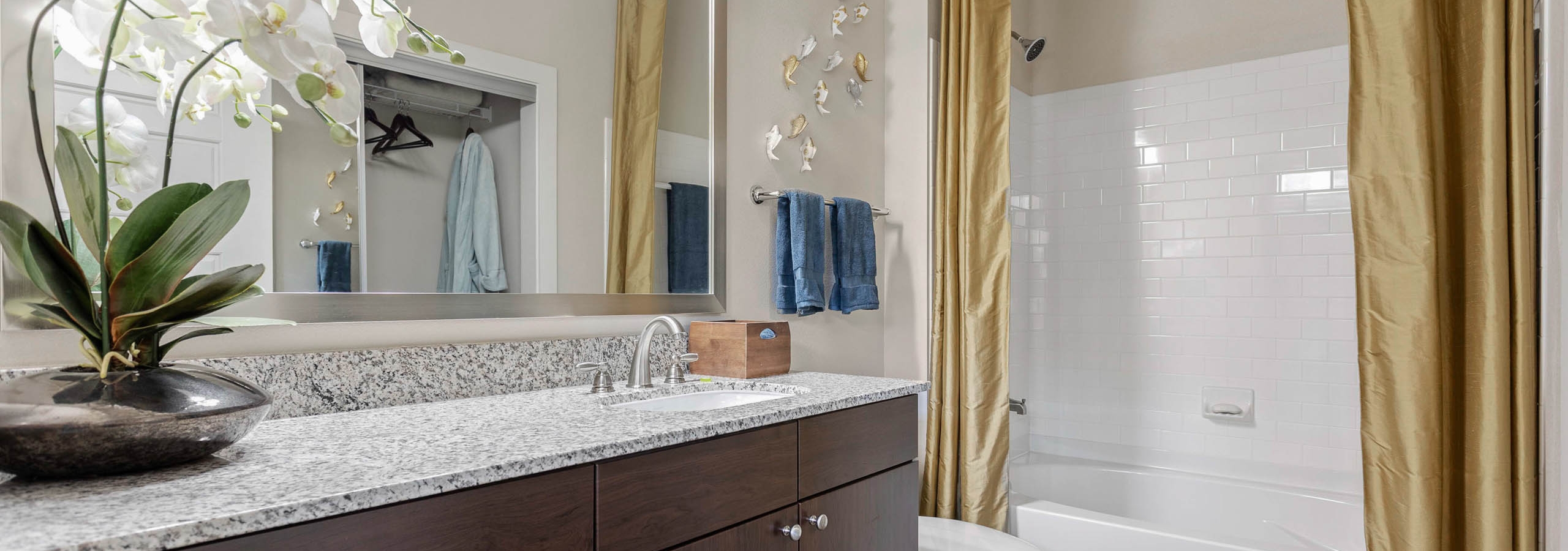 AMLI at Escena apartment bathroom with an orchid on granite countertops and golden shower curtains surrounding a white bath