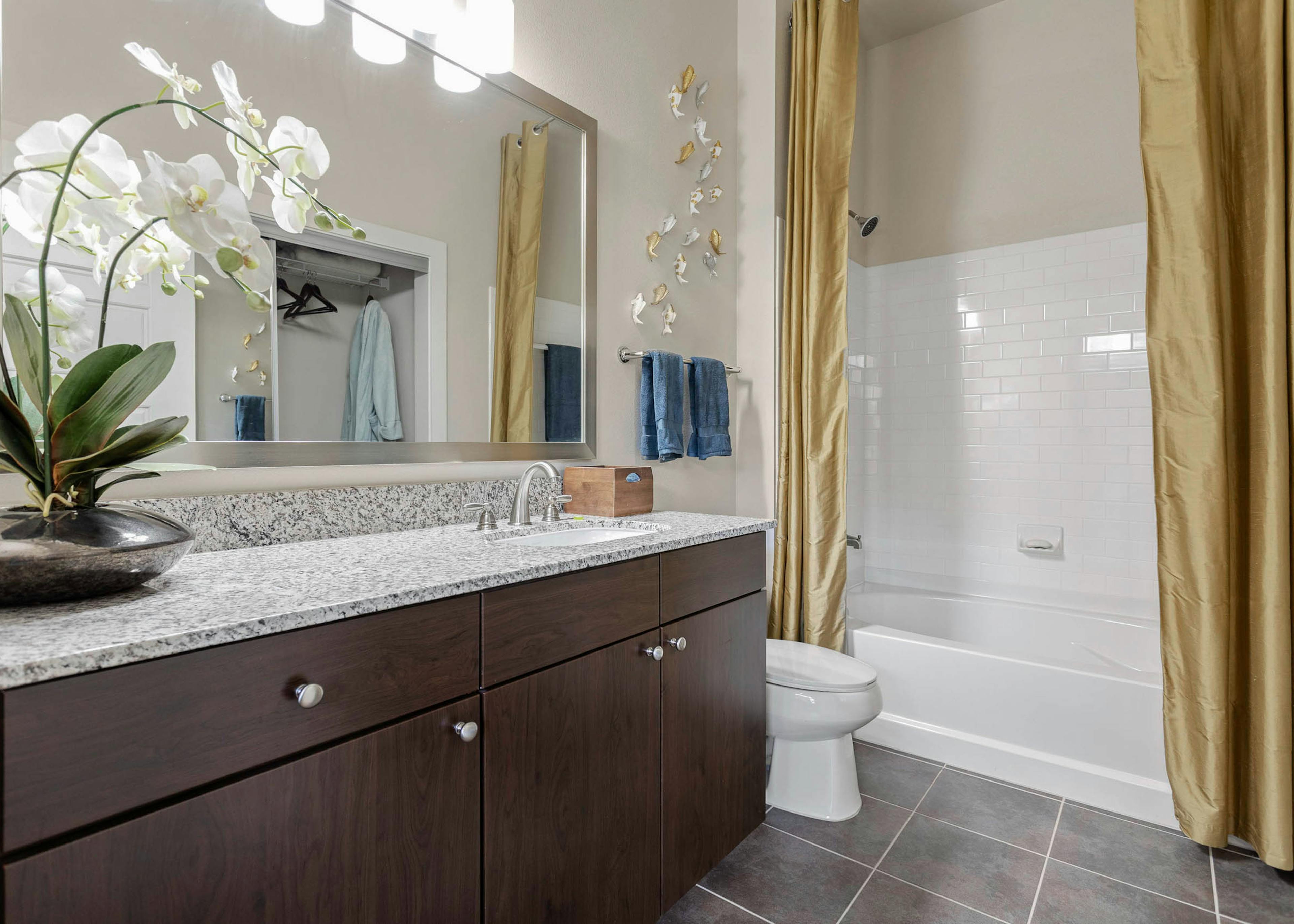 AMLI at Escena apartment bathroom with an orchid on granite countertops and golden shower curtains surrounding a white bath