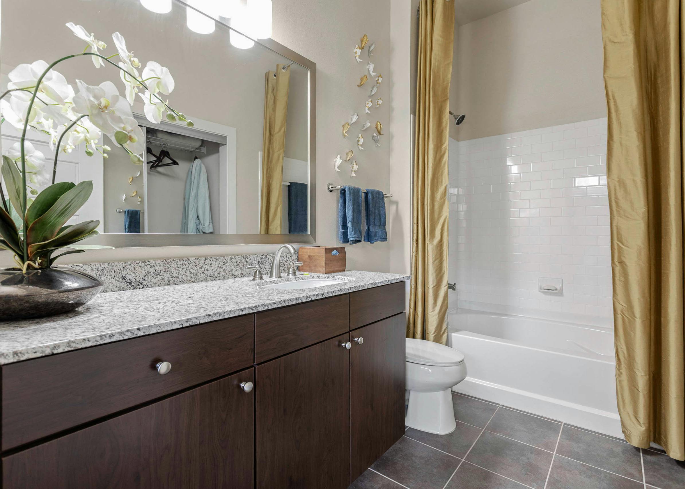 AMLI at Escena apartment bathroom with an orchid on granite countertops and golden shower curtains surrounding a white bath