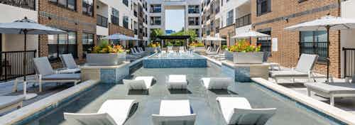 A sunlit shallow pool at AMLI Quadrangle apartments with lounge seating with shading umbrellas and flowers in metal planters