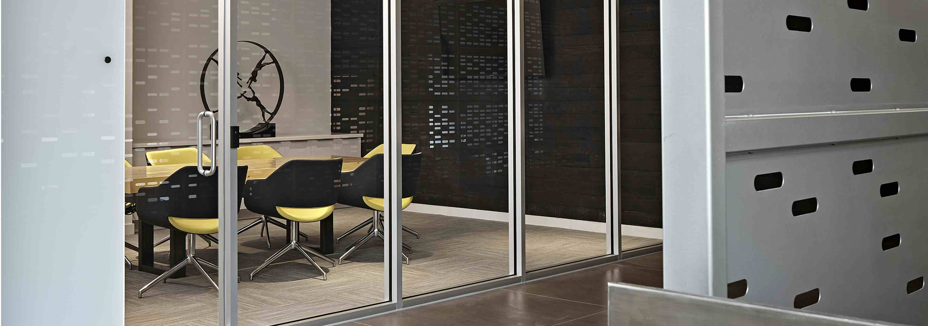 Conference room at AMLI Lofts with a clear glass wall and a conference table paired with bright yellow office chairs