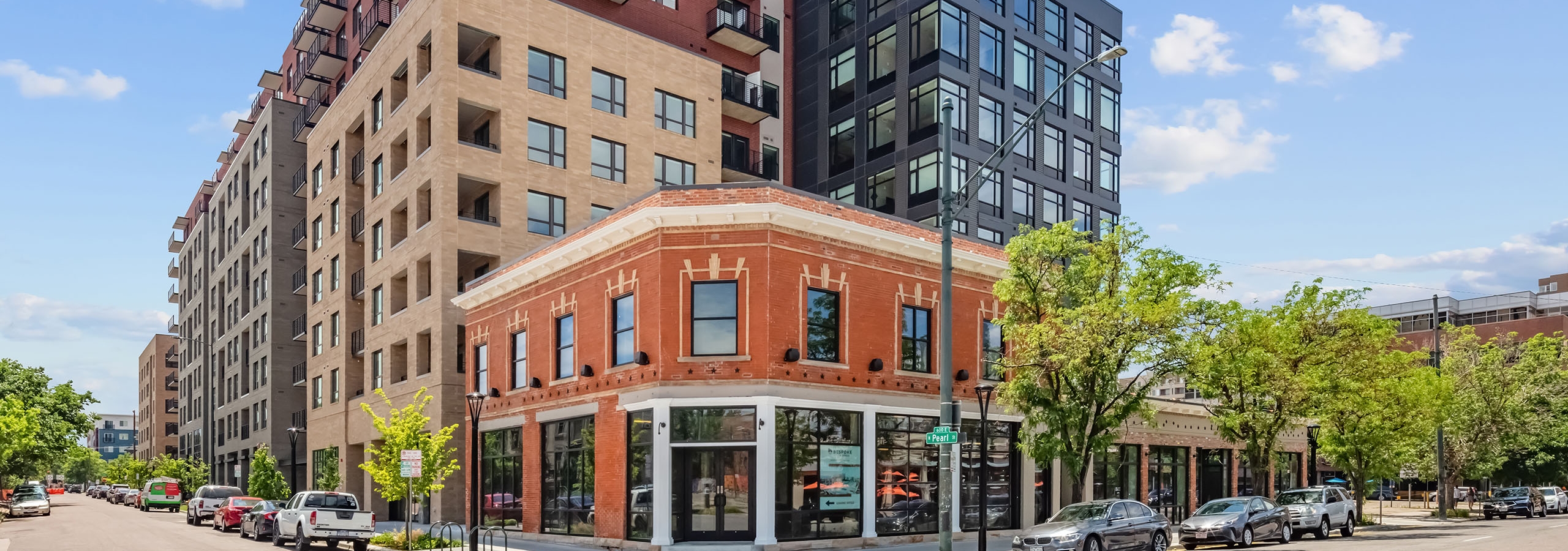 Daytime view of AMLI at Uptown apartment building on the corner of an intersection with colorful of brick and cars parked