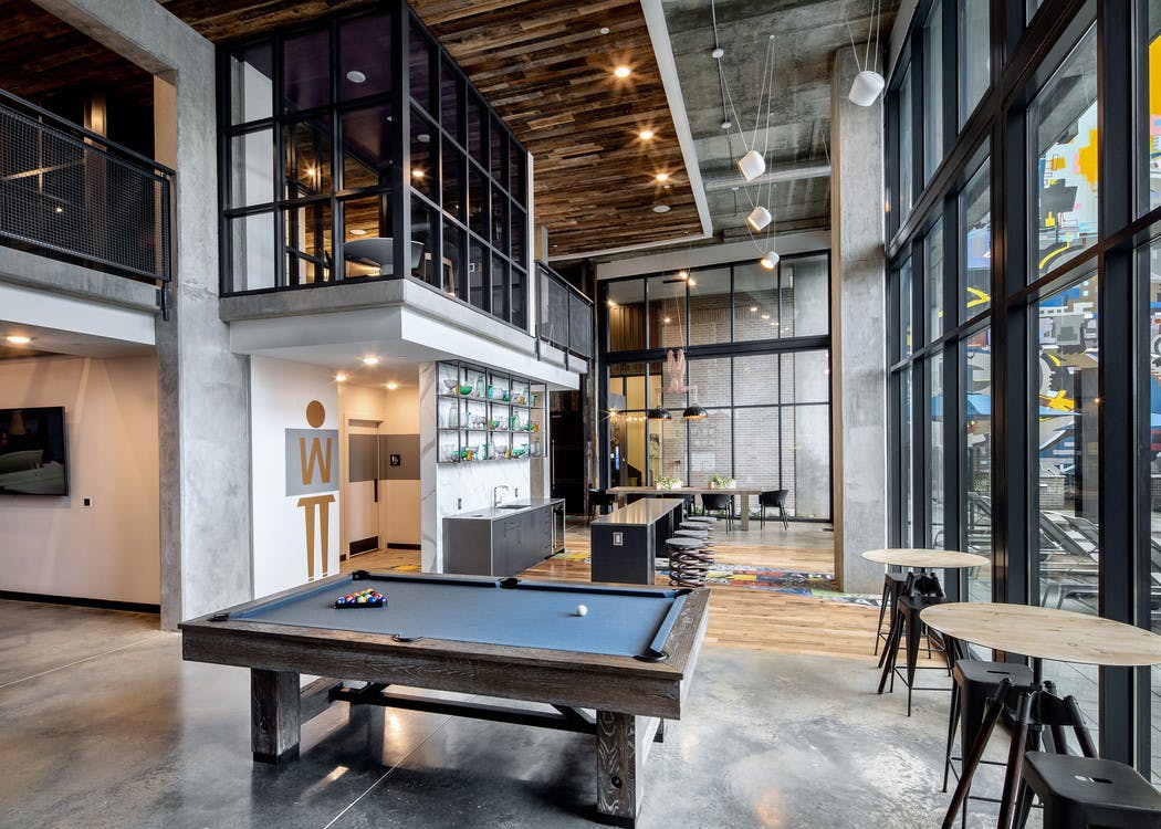 Interior view of AMLI Westside clubroom showing billiards and arcade games with large windows and various seating options
