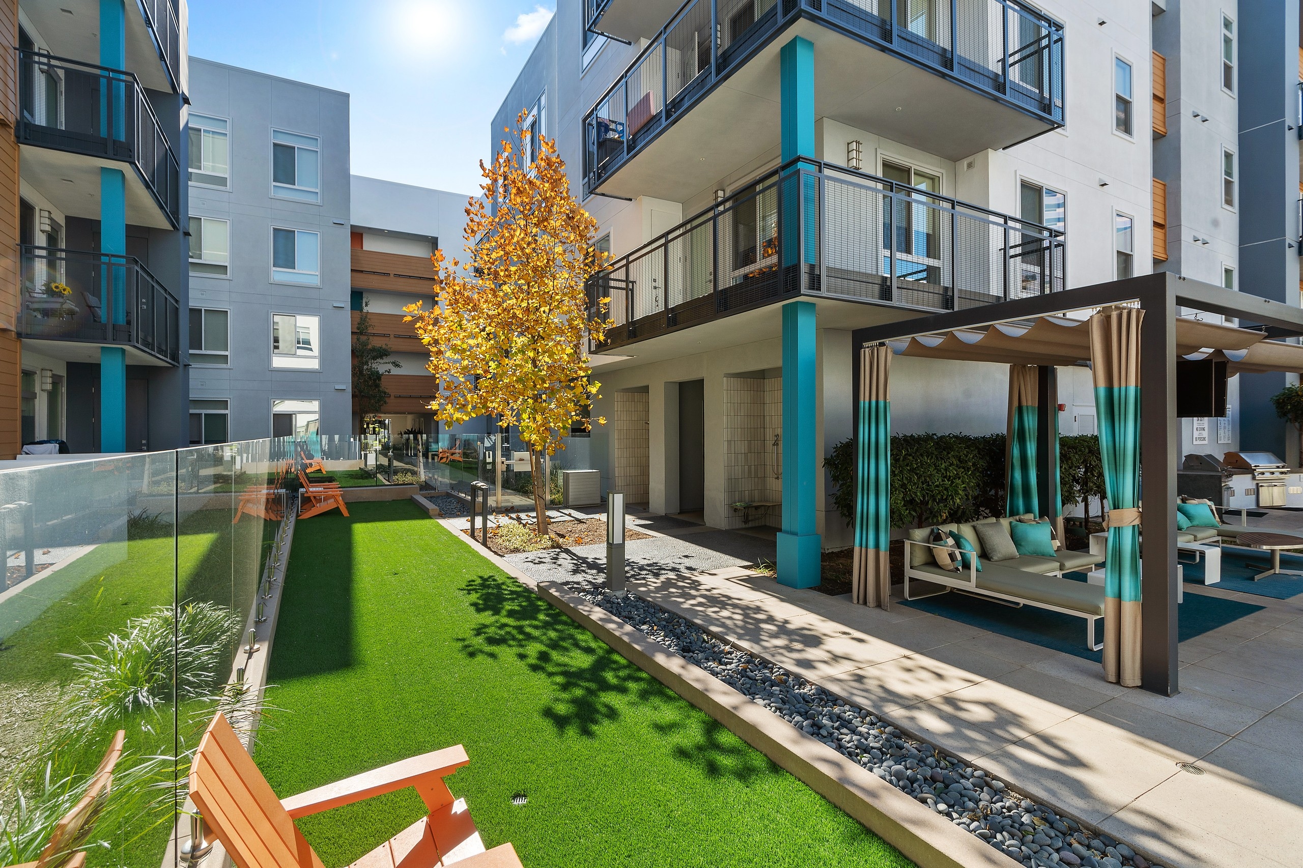Resident leisure area with green turf and orange chairs overlooking poolside cabana and balconies at AMLI Uptown Orange apartments