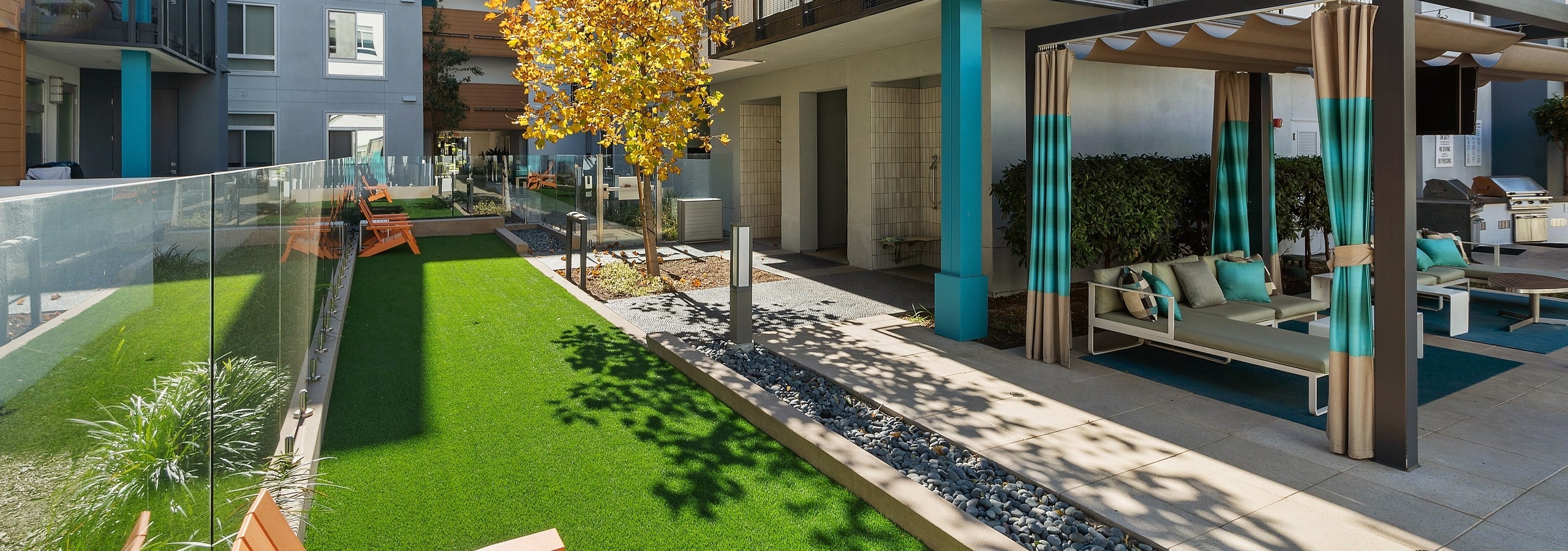 Resident leisure area with green turf and orange chairs overlooking poolside cabana and balconies at AMLI Uptown Orange apartments