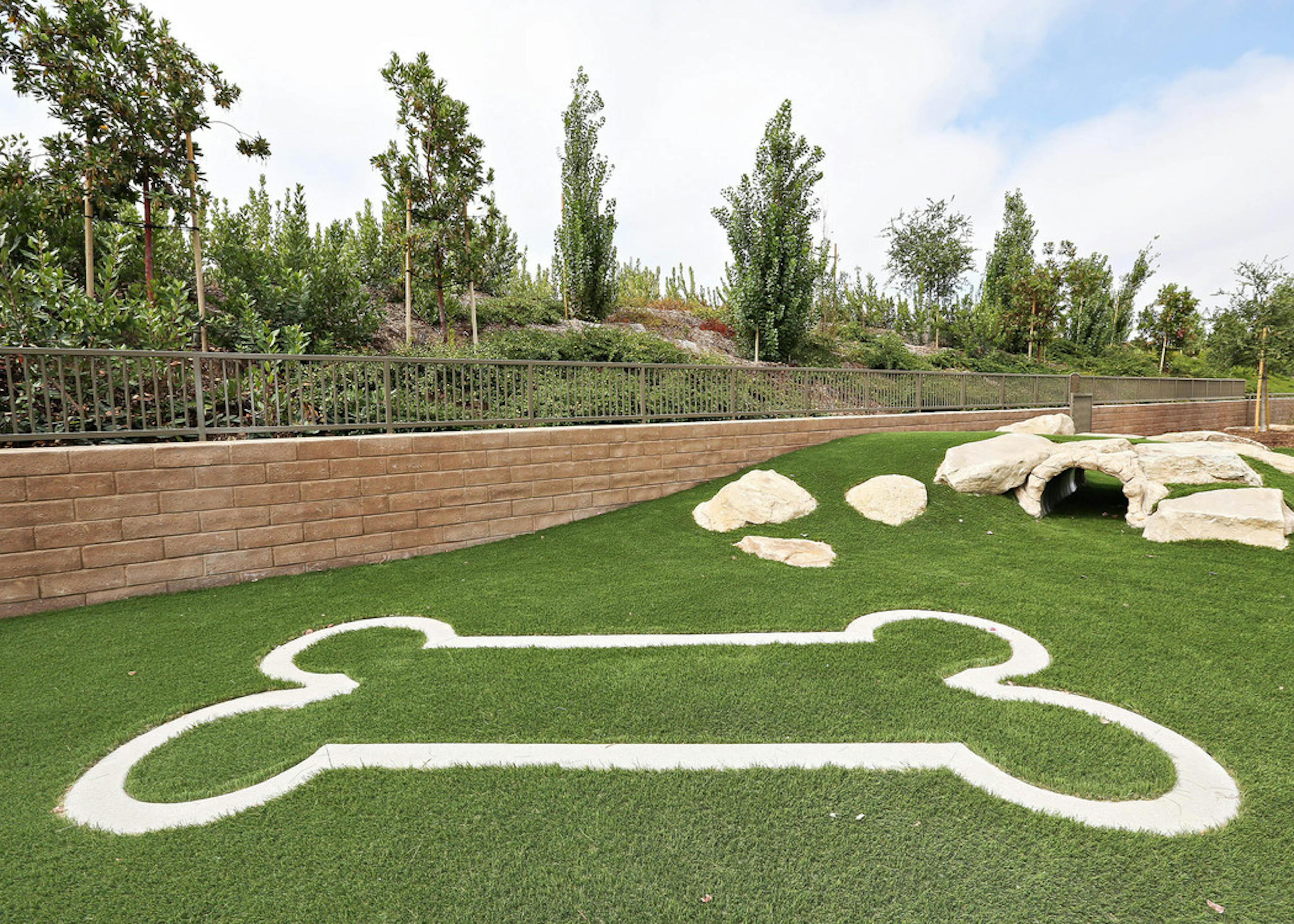 Exterior daytime close-up of pet park at AMLI Spanish Hills apartment with bark log tunnel and bone-shaped design on turf