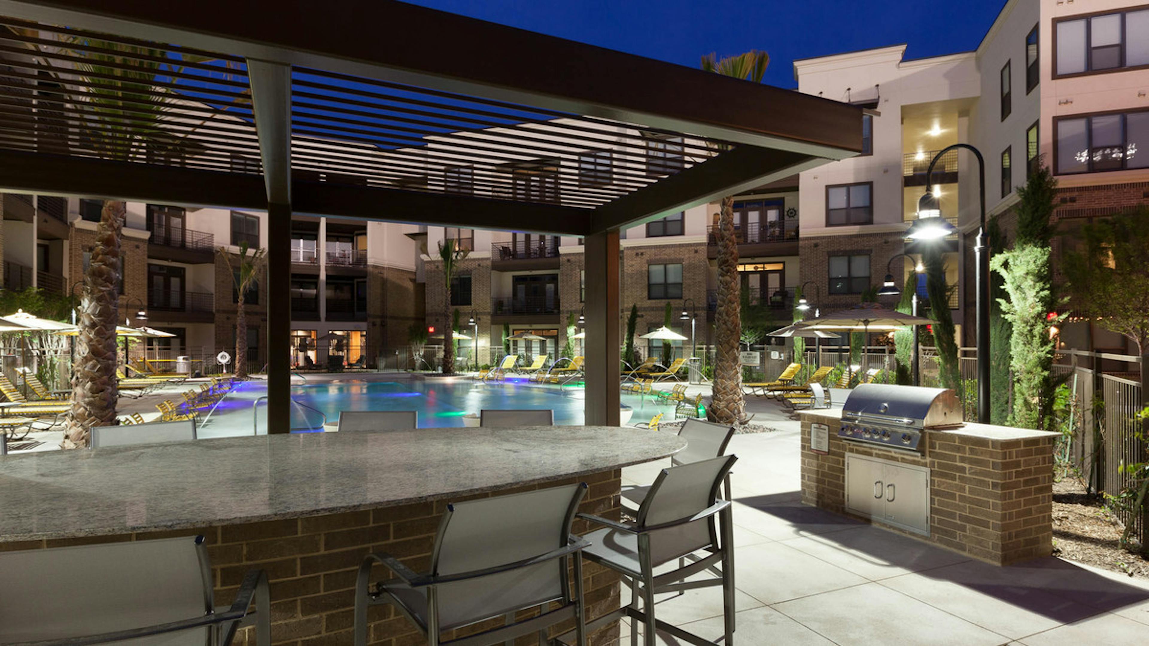 Nighttime view of grill station, seating and pool area at AMLI at the Ballpark apartments with buildings in background