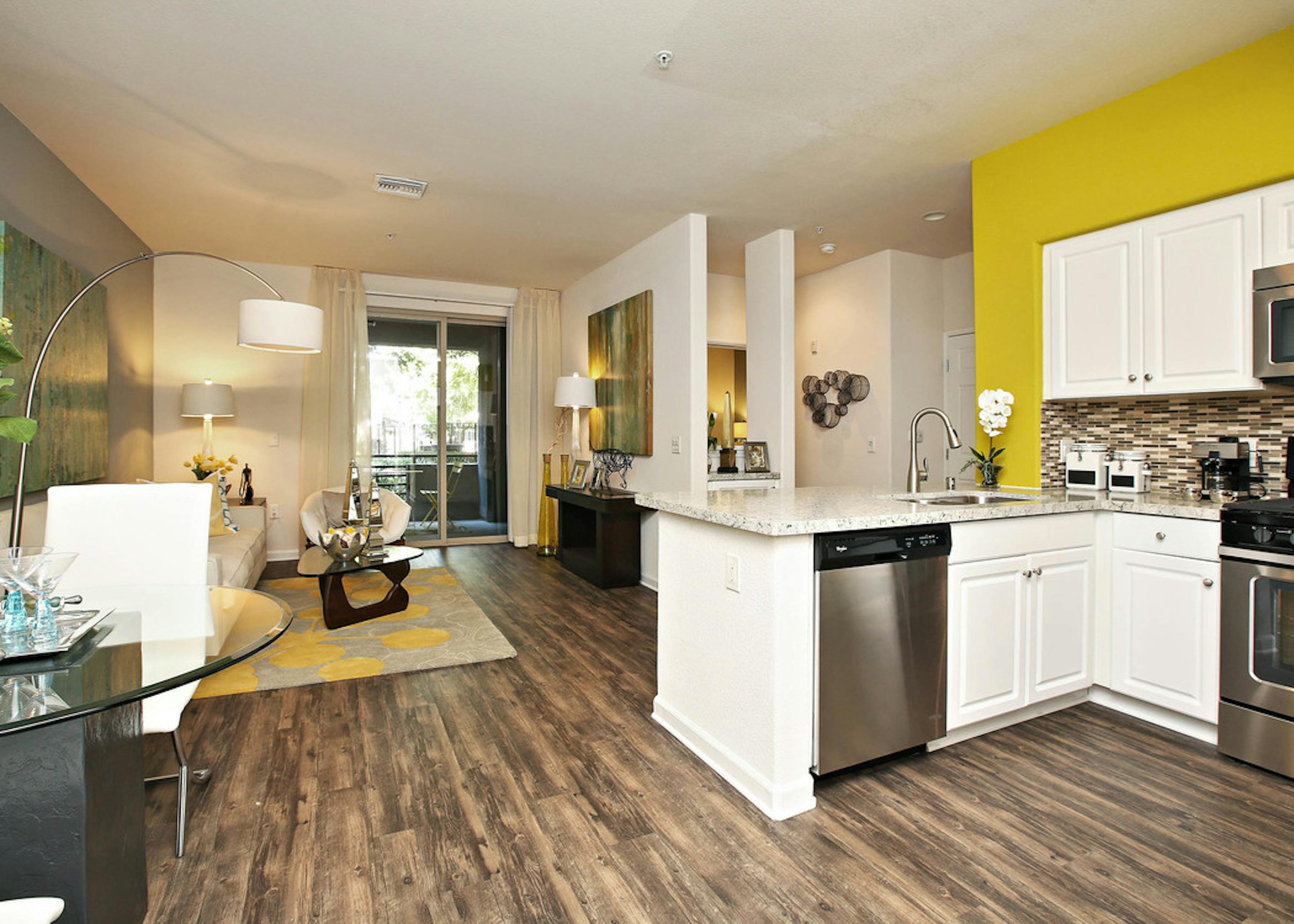 Interior of AMLI Warner Center kitchen and furnished living room with hard wood floors, white couch and centered wall art 