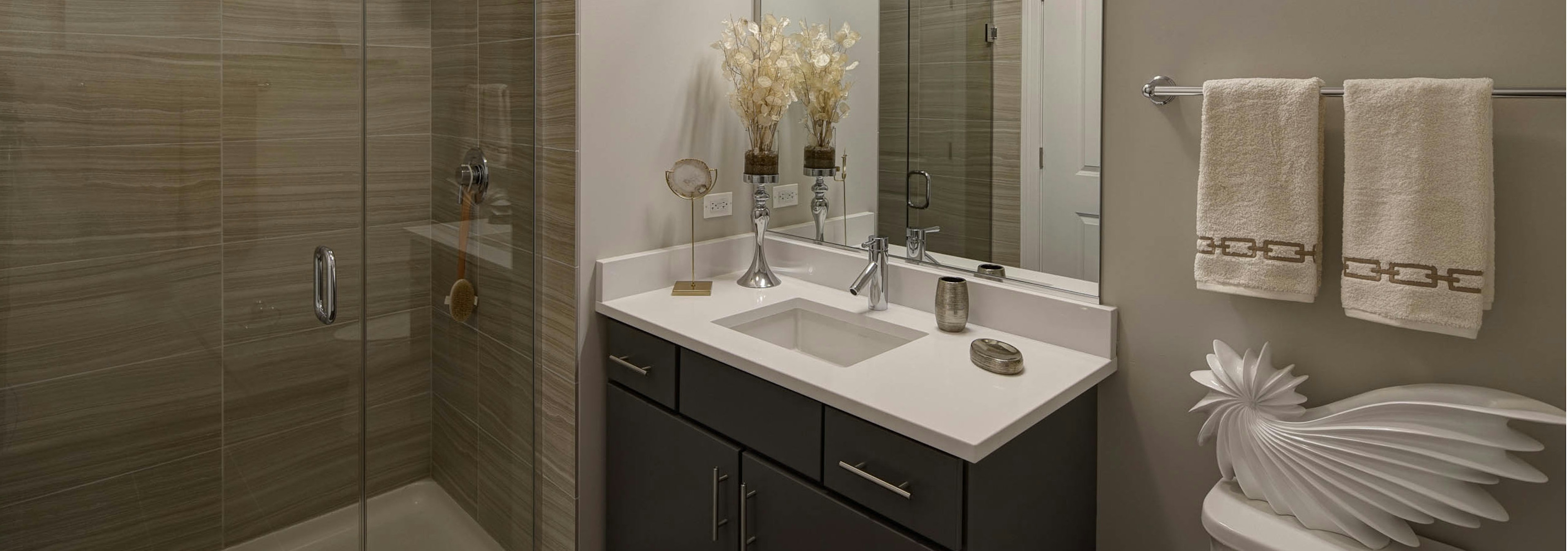 Bathroom at AMLI Lofts with taupe decor and a single vanity as well as a beige tiled shower with a clear glass door