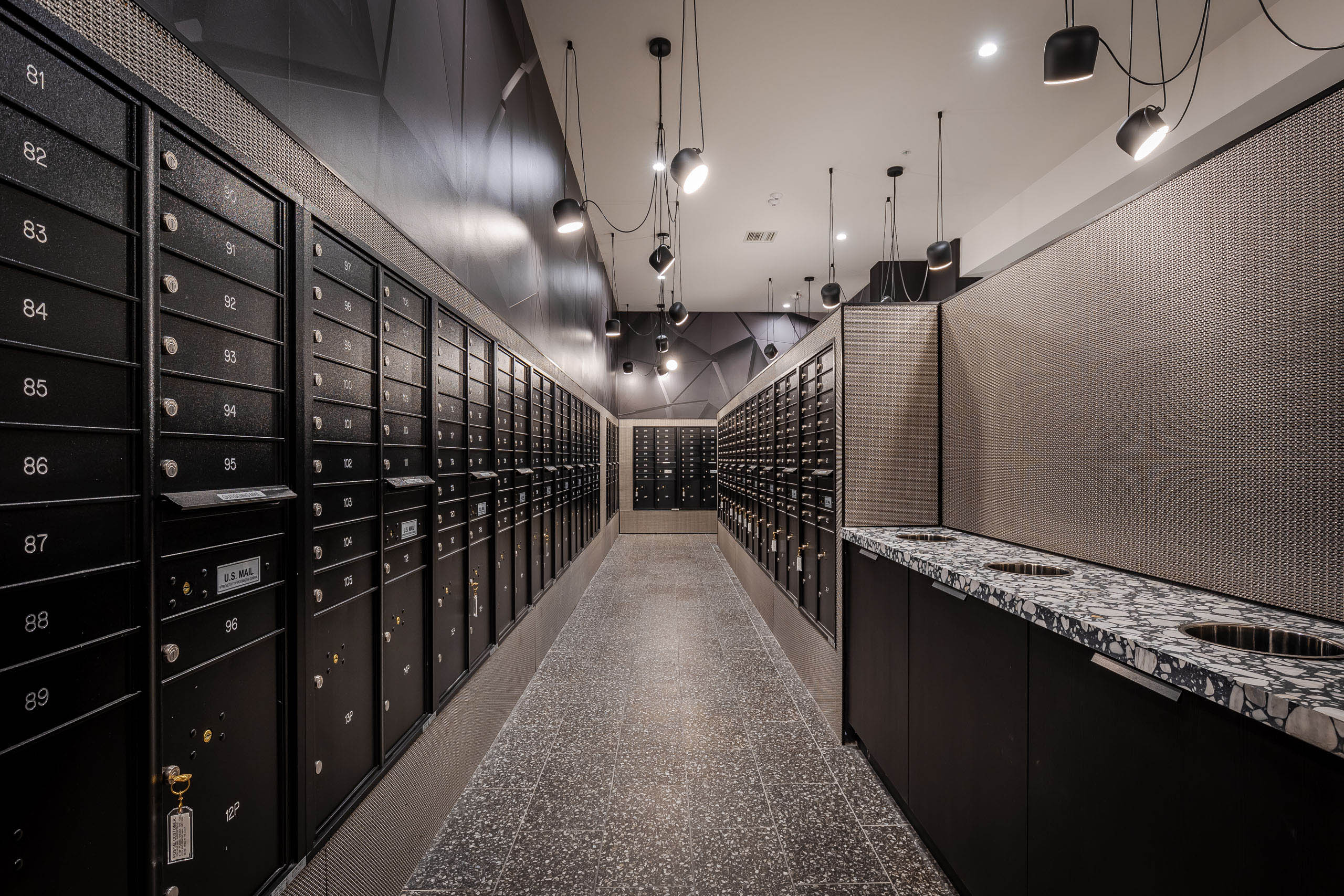 Interior view of the AMLI Midtown Miami mailroom with black mailboxes lining the walls and black and white speckled floor 