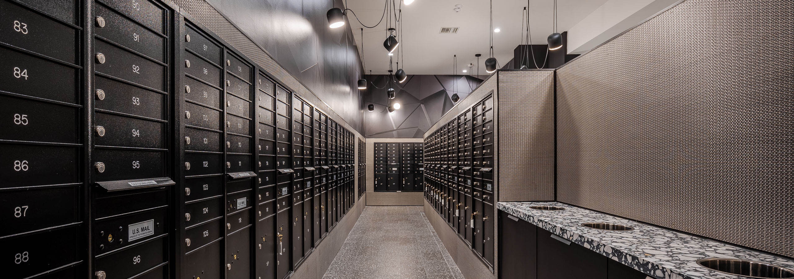 Interior view of the AMLI Midtown Miami mailroom with black mailboxes lining the walls and black and white speckled floor