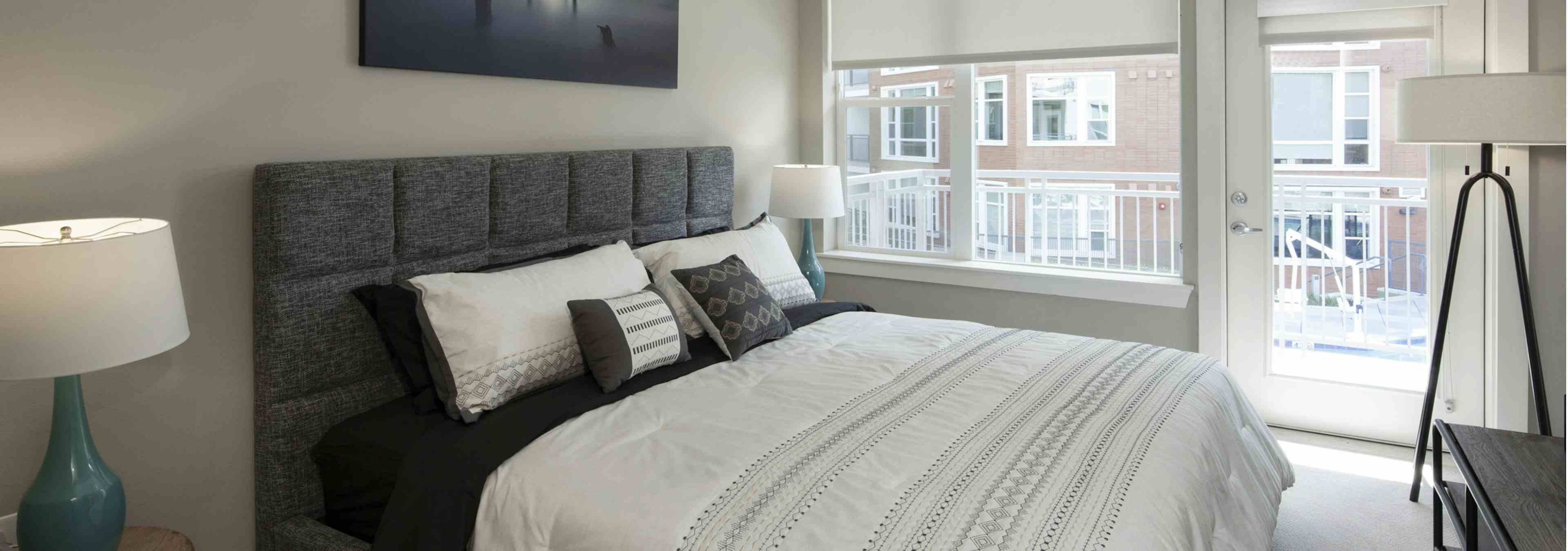 Interior view of AMLI Riverfront Green apartment bedroom and lamps with window views of adjacent brick apartment building