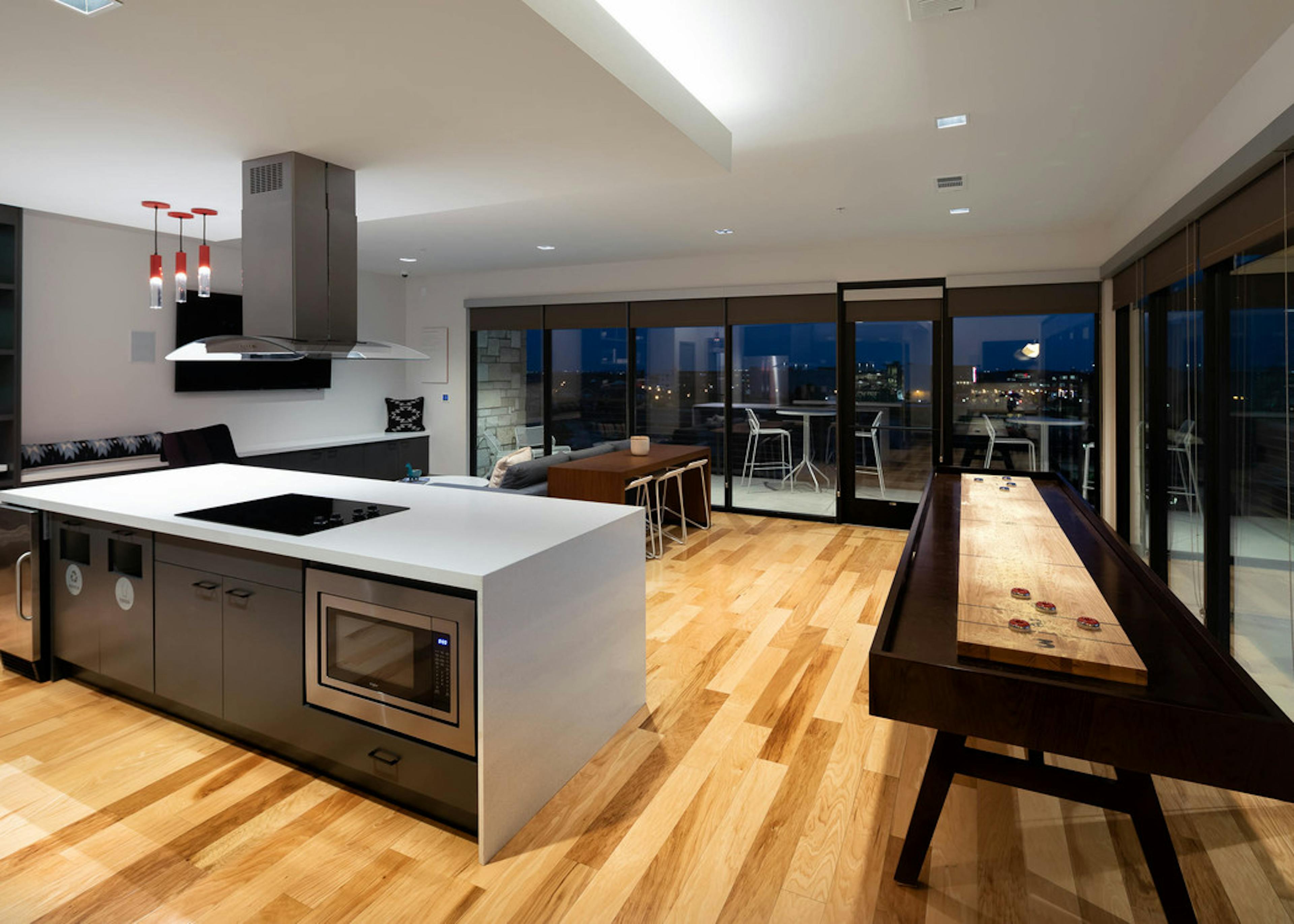 Clubroom at AMLI on Aldrich with floor to ceiling windows showing nighttime view with light wood floors and spacious kitchen