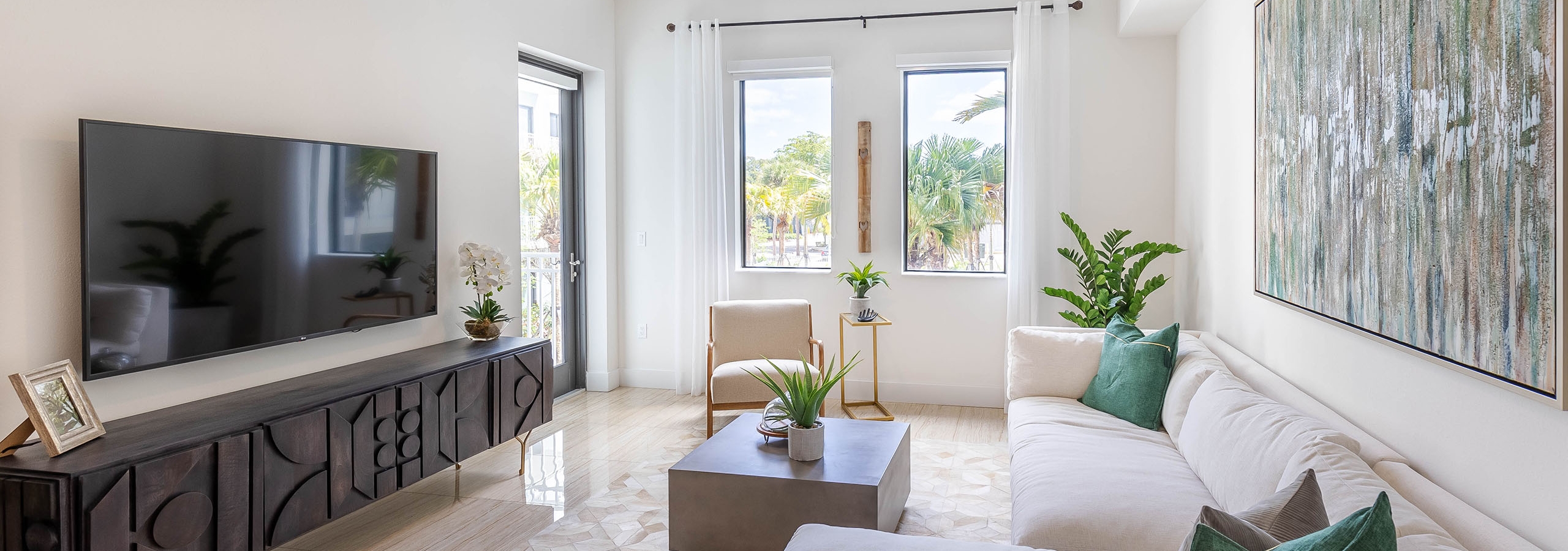 Interior view of an AMLI Park West apartment living area with white sectional sofa and coffee table and TV and 2 windows
