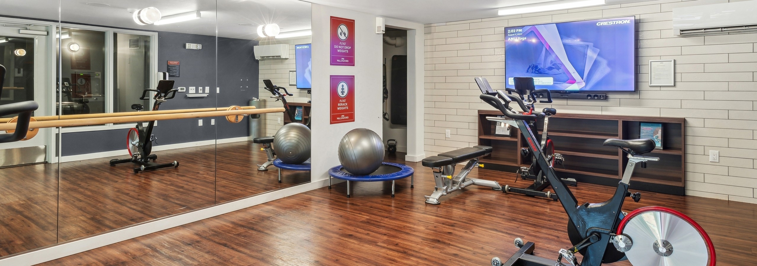 Spin yoga room at AMLI Wallingford with hardwood flooring and full length mirror and a stationary bike and television