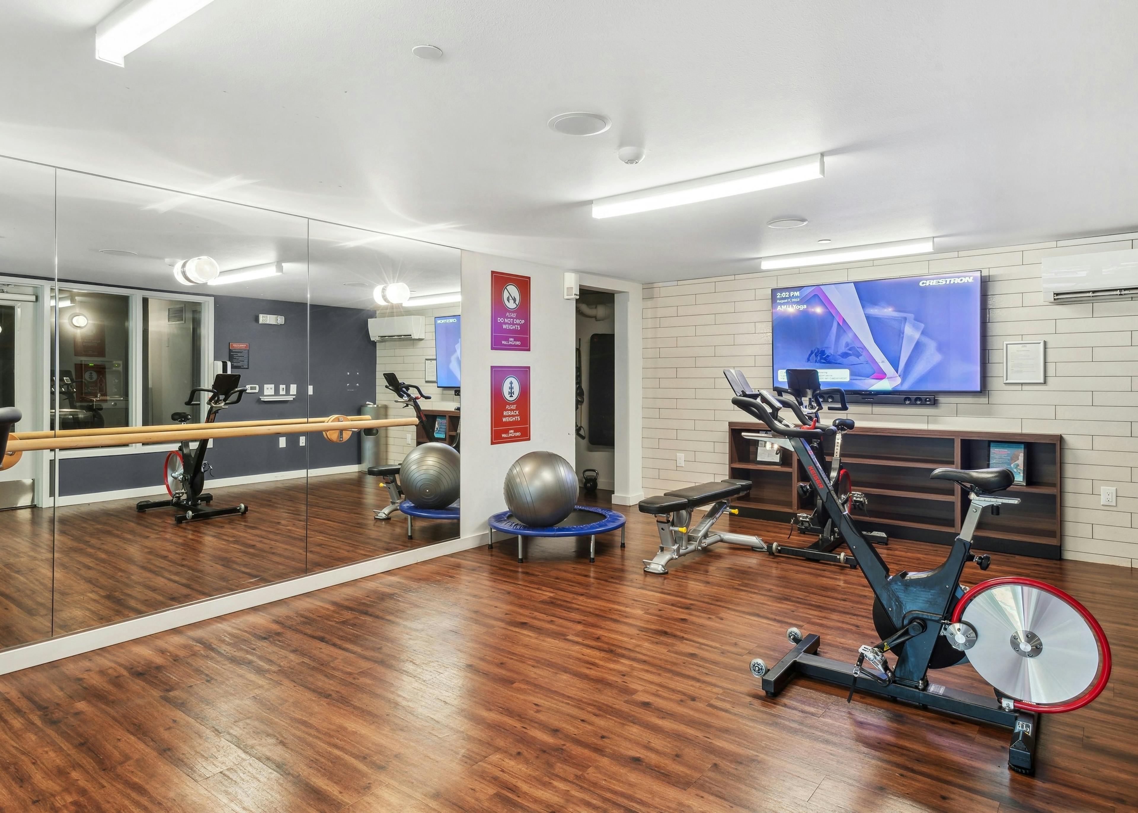 Spin yoga room at AMLI Wallingford with hardwood flooring and full length mirror and a stationary bike and television 