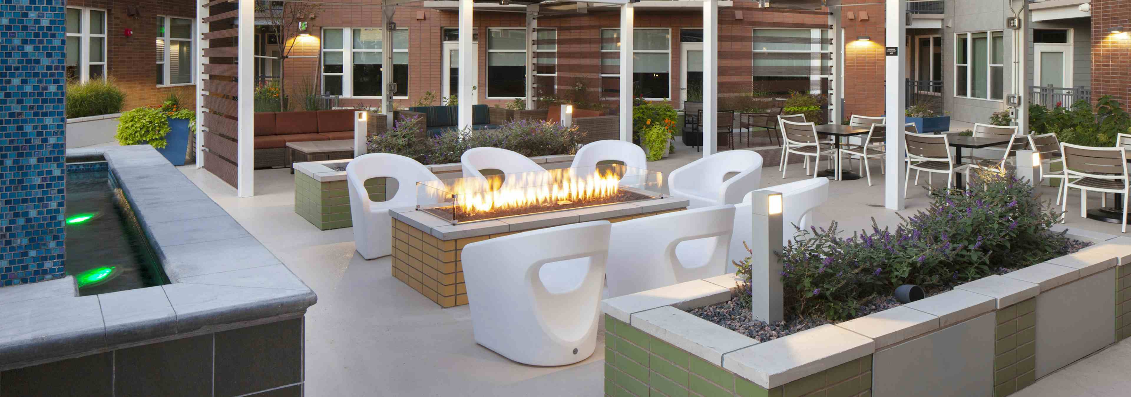 Night time view of rooftop area at AMLI Riverfront Green apartments with fire pit featured with chairs and planter boxes